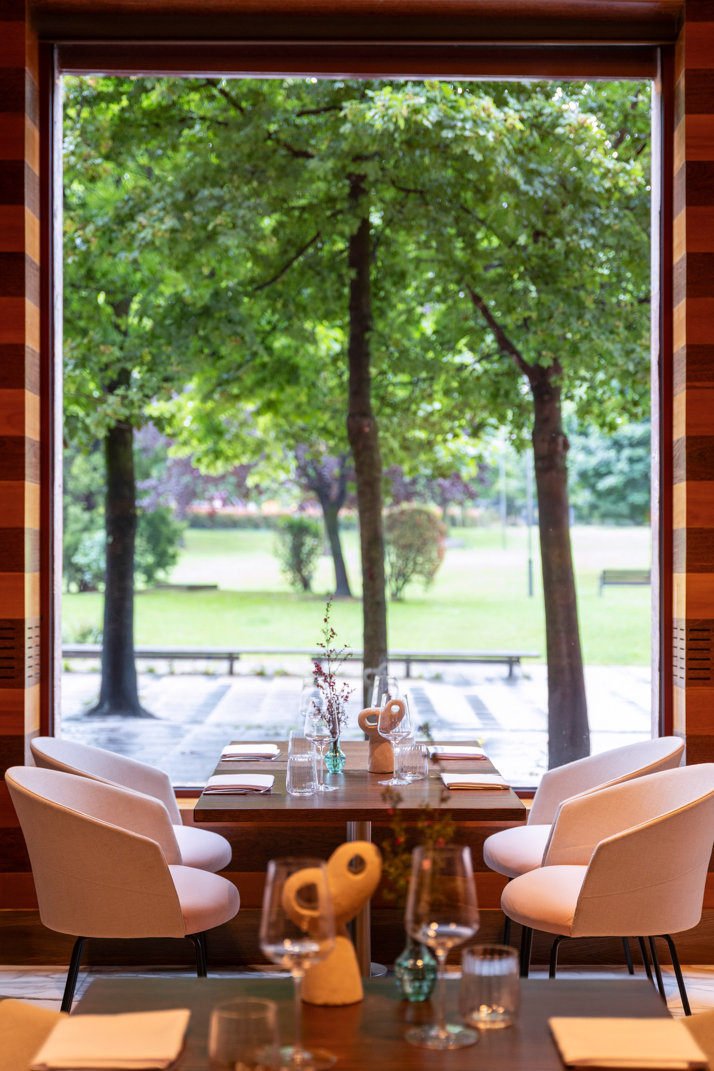 Modern dining table and chairs by window with green park view.