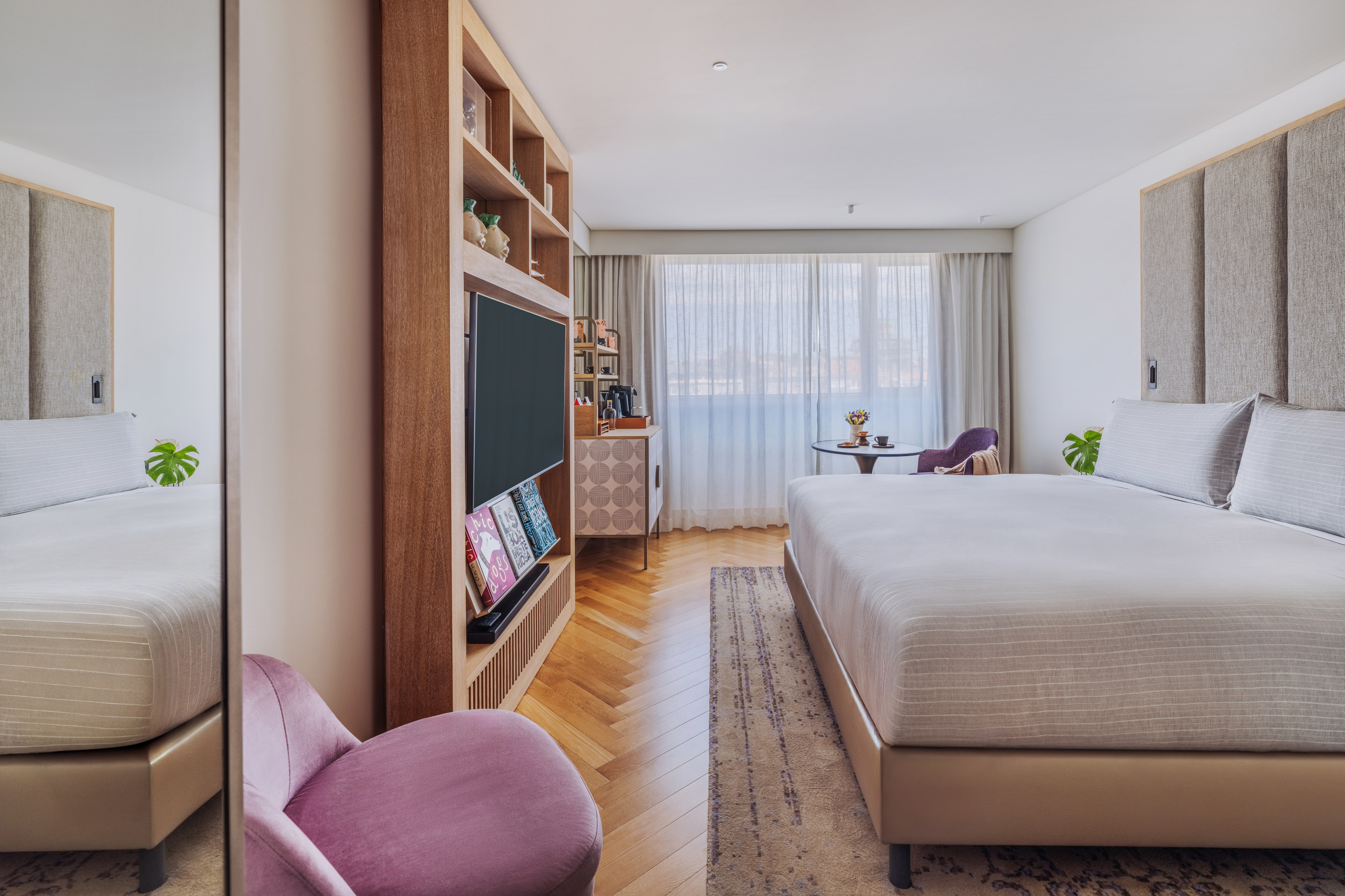 Modern hotel room with large bed, wood floor, TV, and window.