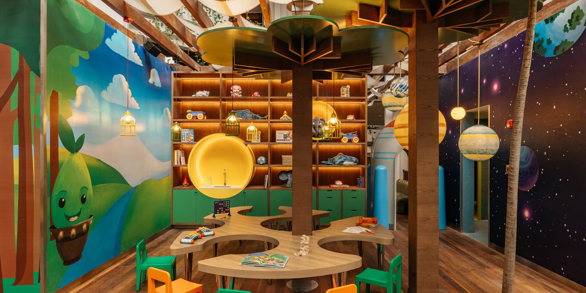 Colorful kids' play area with tree decor, space mural, toys, and activity tables.