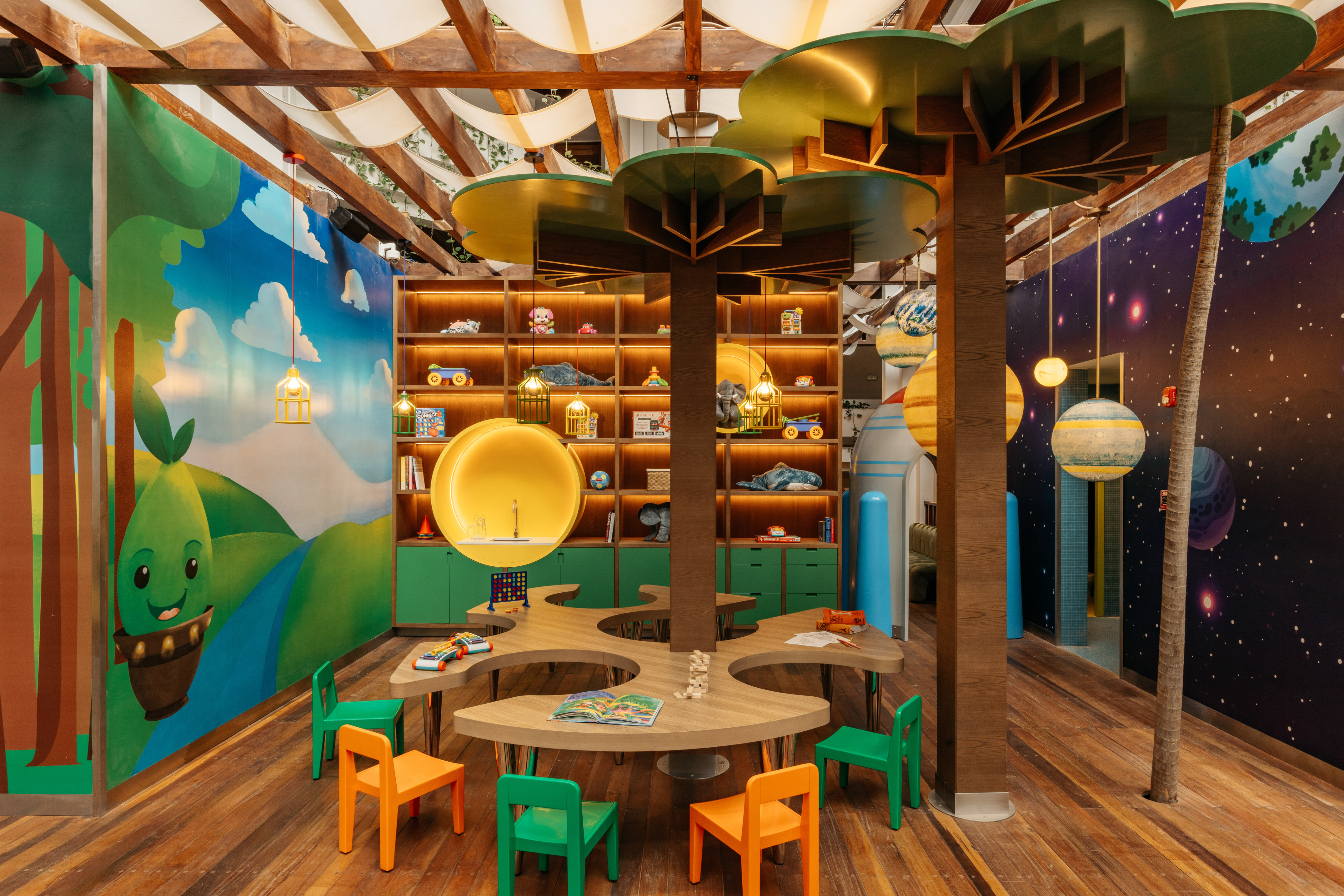 Vibrant kids play zone with tree tables, toy shelves, and nature/space themed murals.