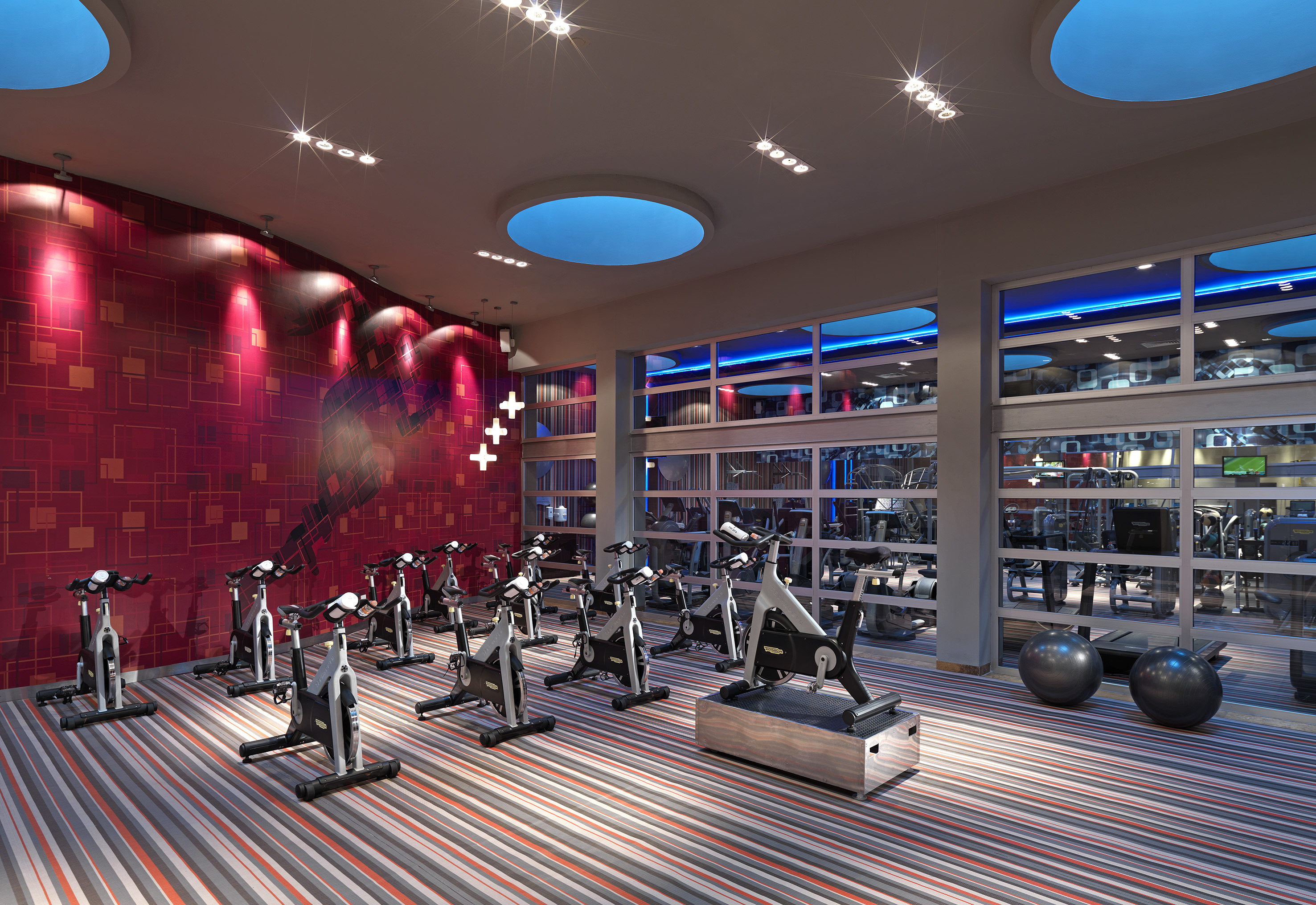 Modern spin class studio with exercise bikes, red patterned wall, and blue lights.