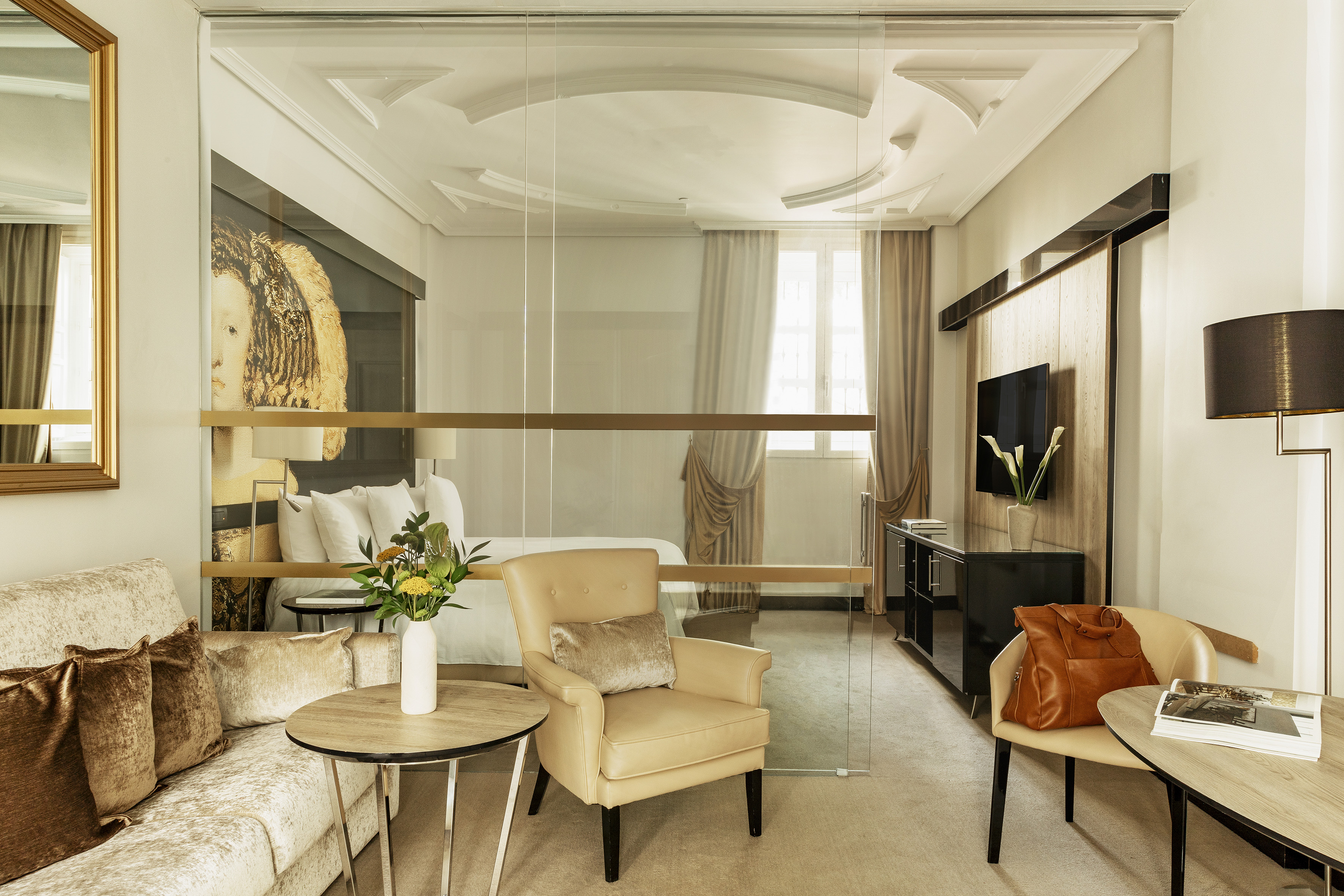 Elegant hotel suite with glass partition, living area, and modern bedroom.