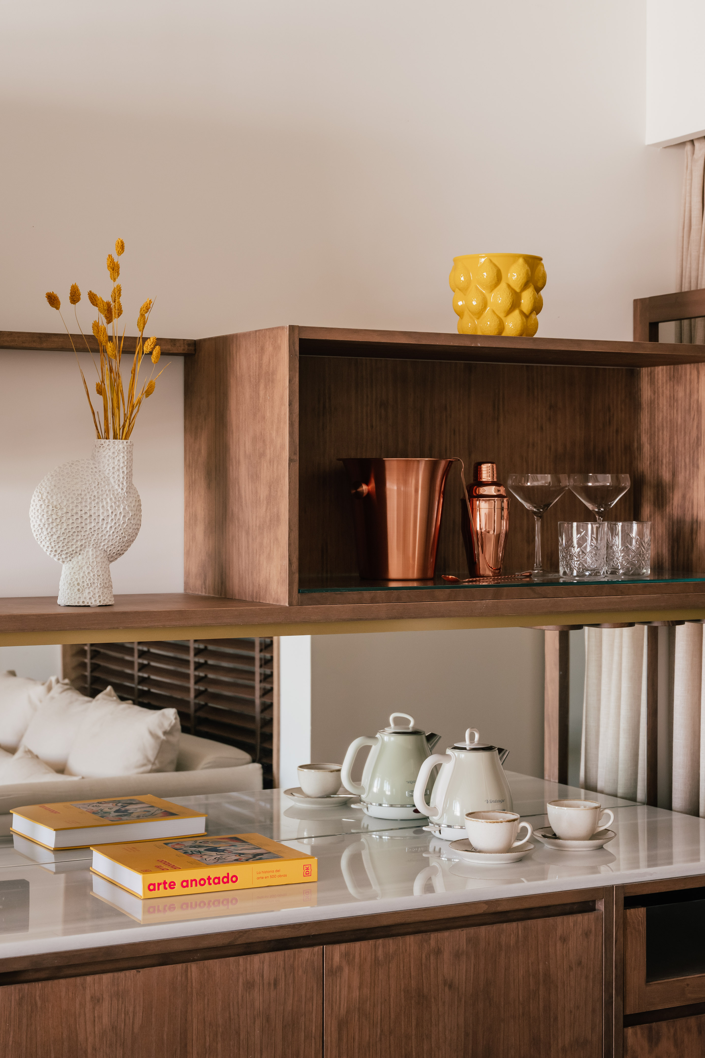 Styled wooden shelves featuring copper barware, coffee kettles, textured vase, and art books.
