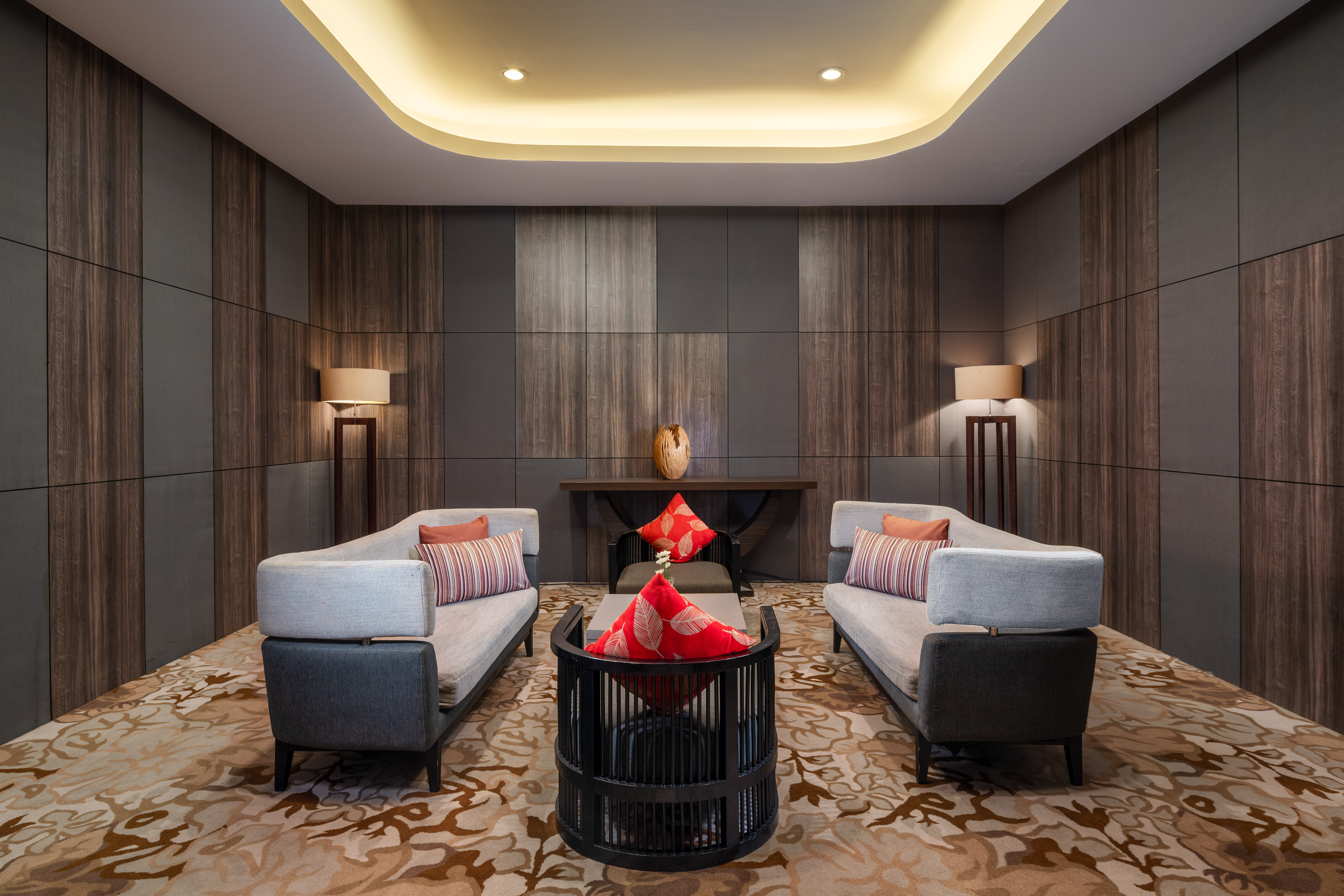 Modern lounge area with grey sofas, patterned rug, and dark wood panel walls.