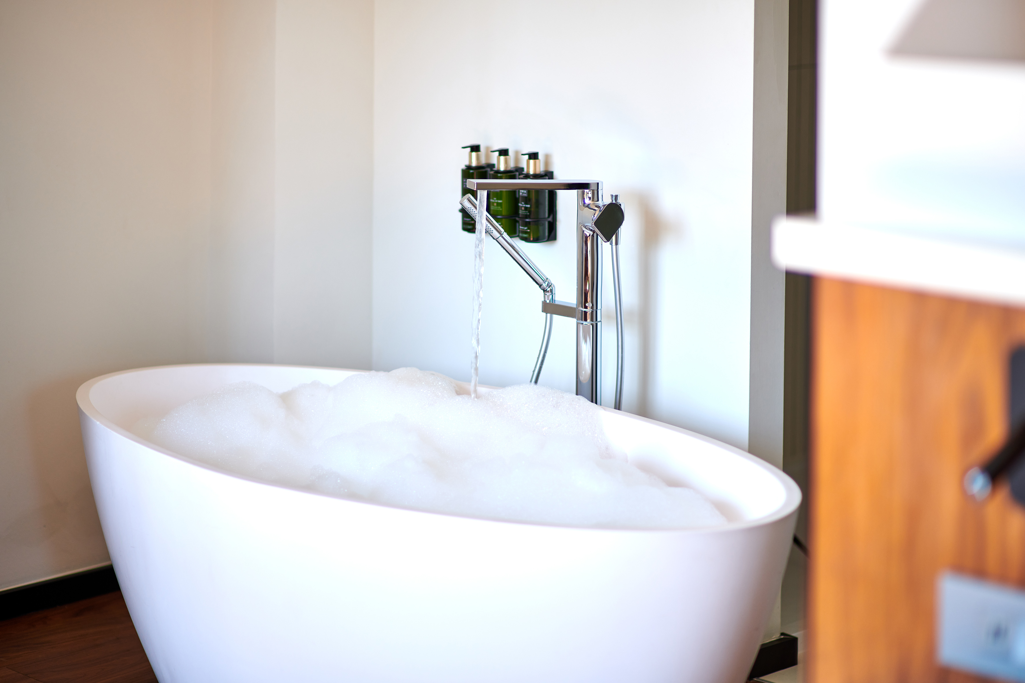 Modern freestanding bathtub with bubbles, water flowing from chrome faucet.