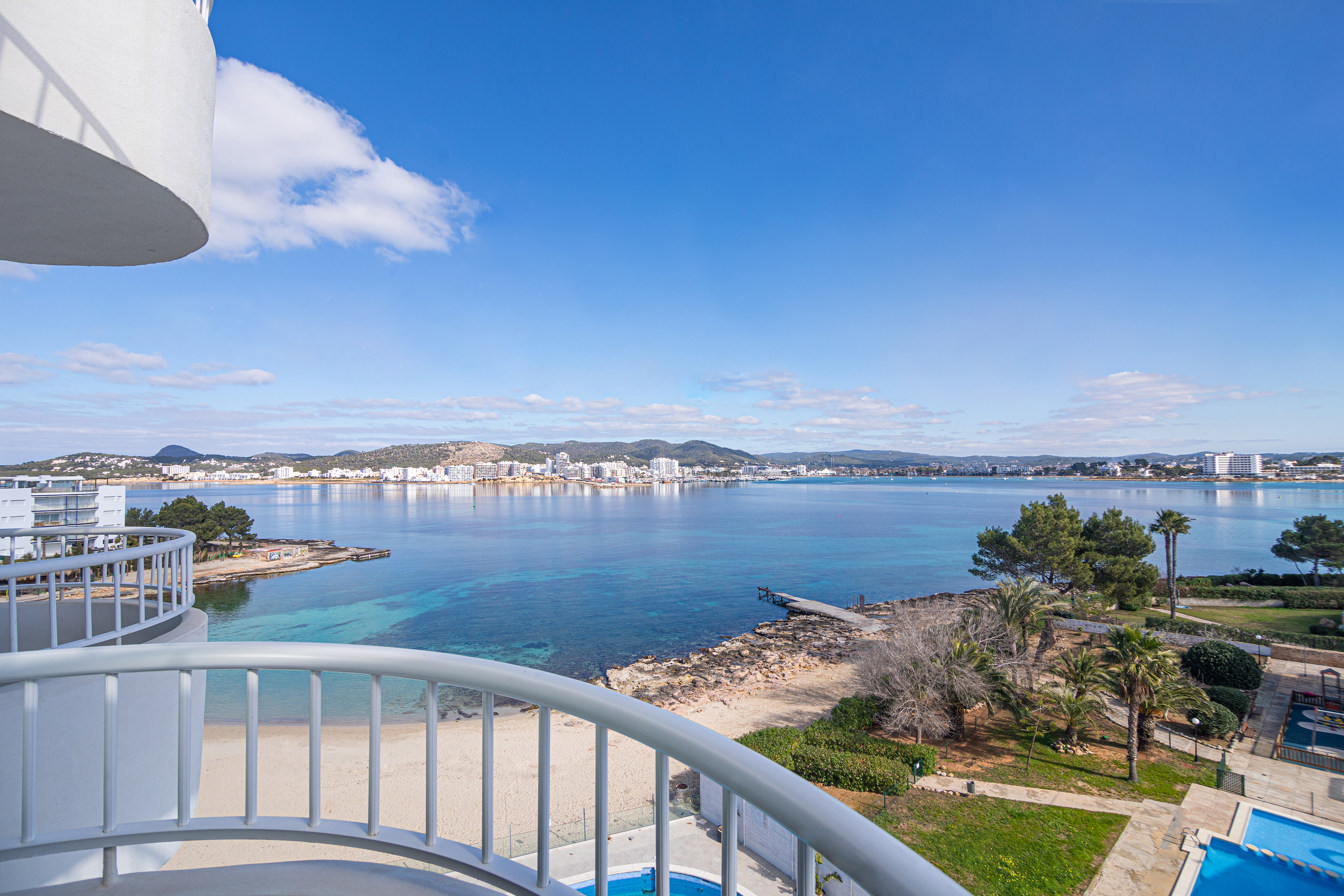 Balcony view: clear blue sea, sandy beach, distant coastal city skyline.