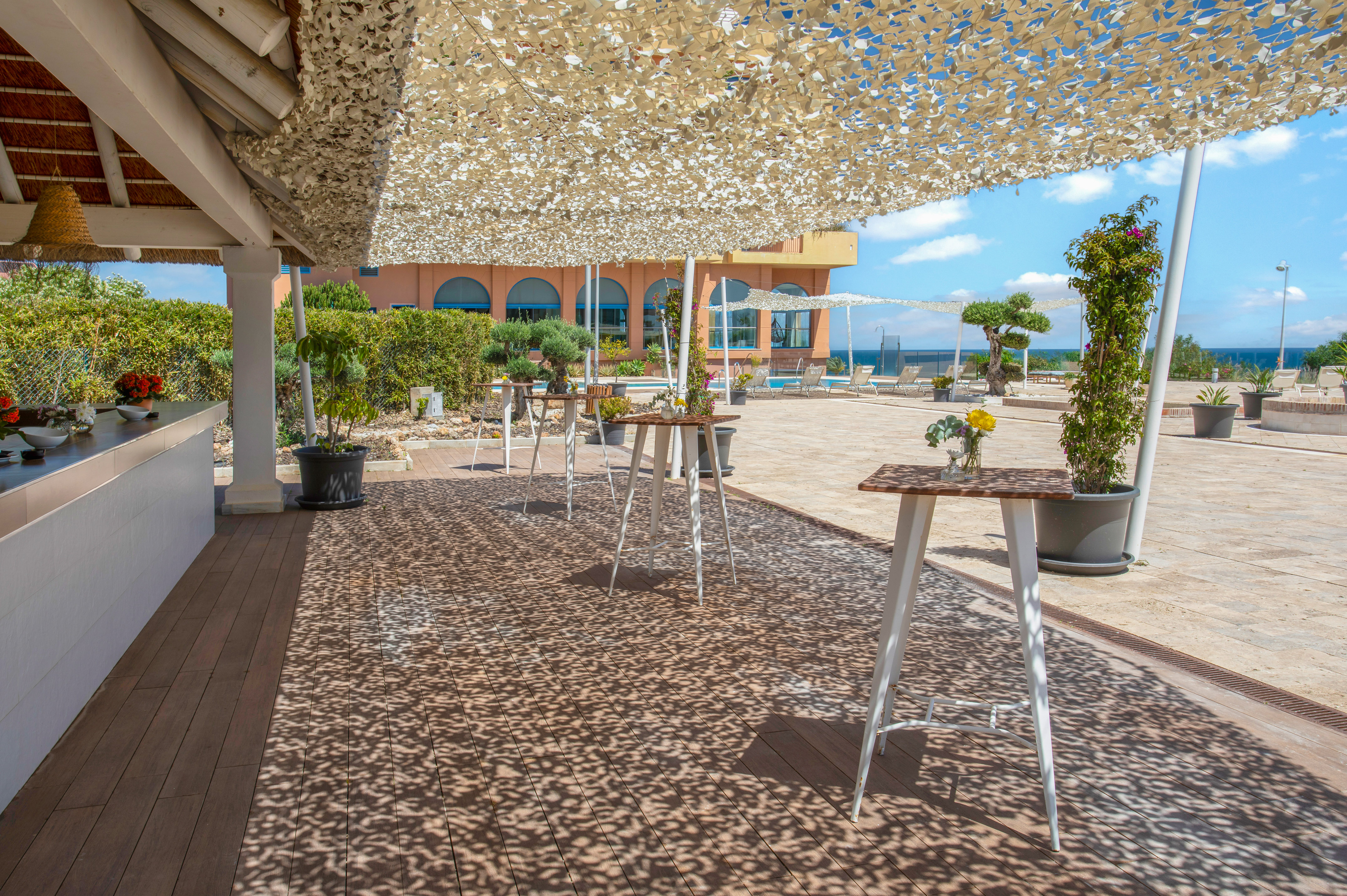 Resort patio with shade canopy, cocktail tables, bar, pool, and ocean view.