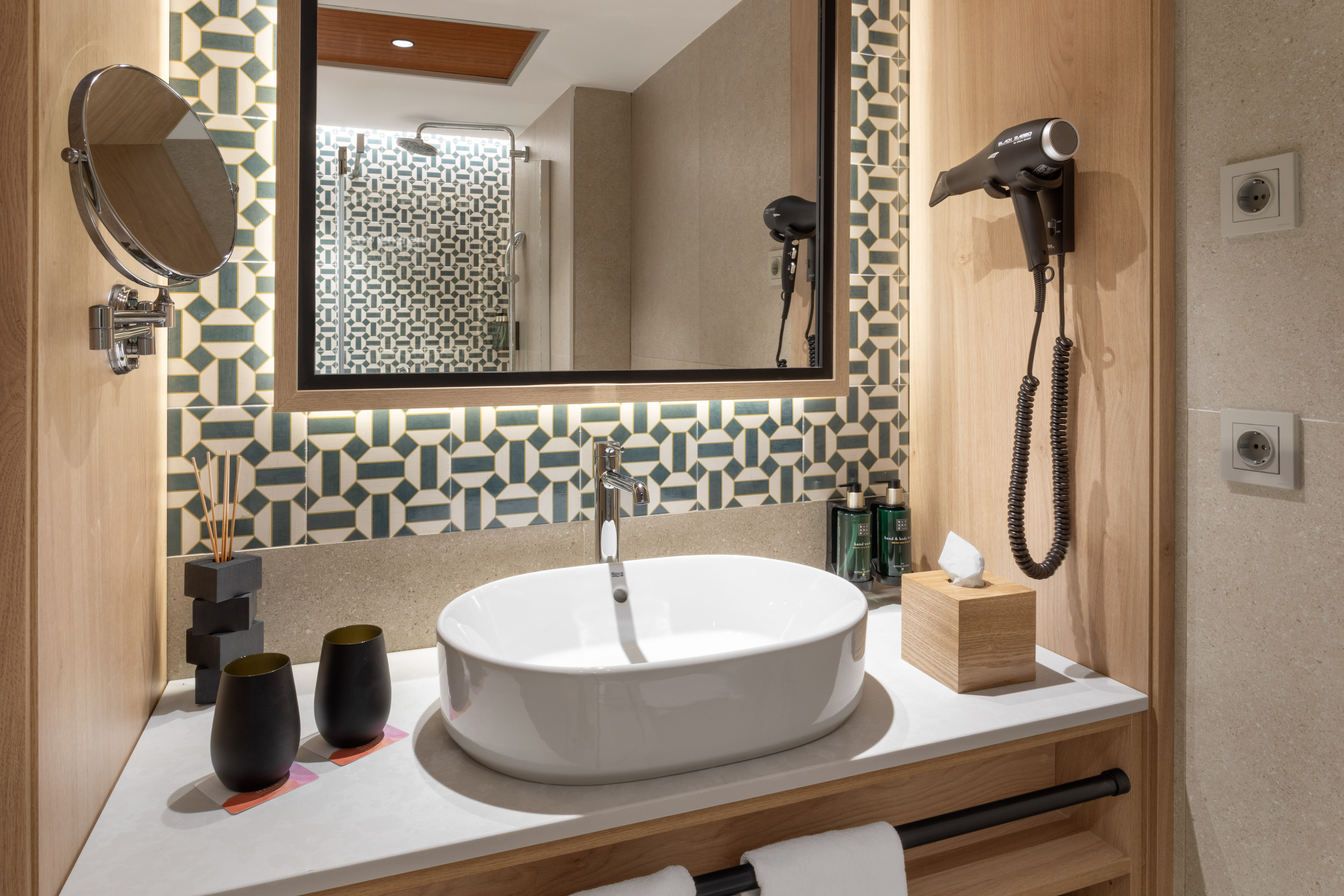 Modern hotel bathroom vanity with oval sink, large mirror, and geometric tiles.