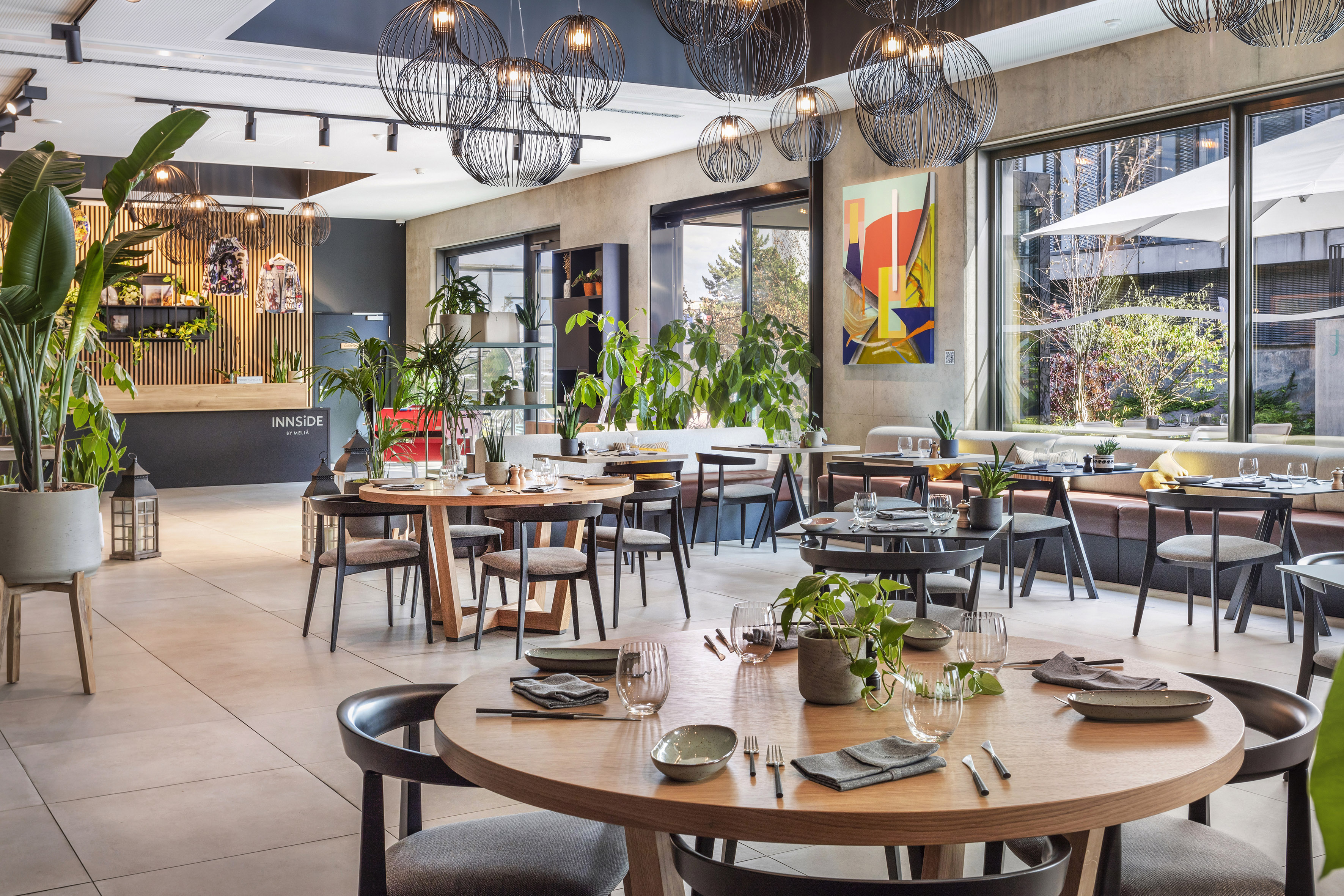 Modern hotel restaurant interior with tables, plants, and statement lighting. - De Gaart, Cuisine locale - INNSiDE Luxembourg, Luxembourg