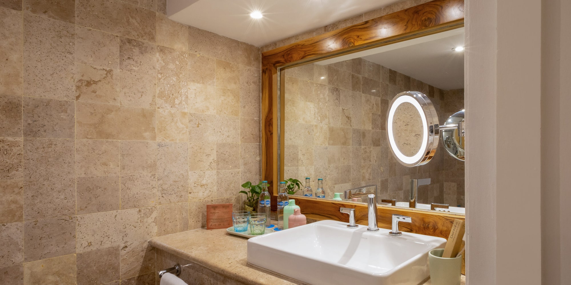 Baño moderno, tocador con lavabo blanco, espejo de madera y azulejos de piedra.