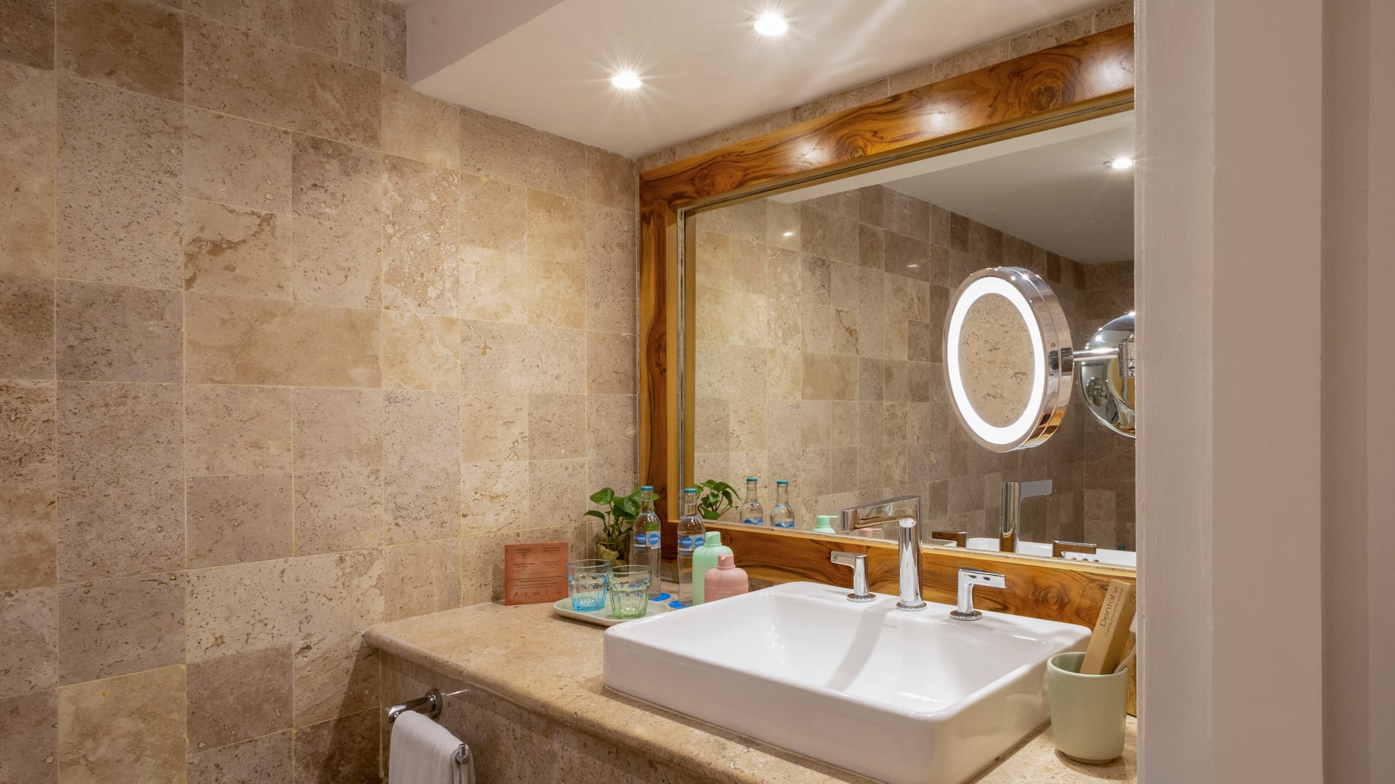 Baño moderno, tocador con lavabo blanco, espejo de madera y azulejos de piedra.