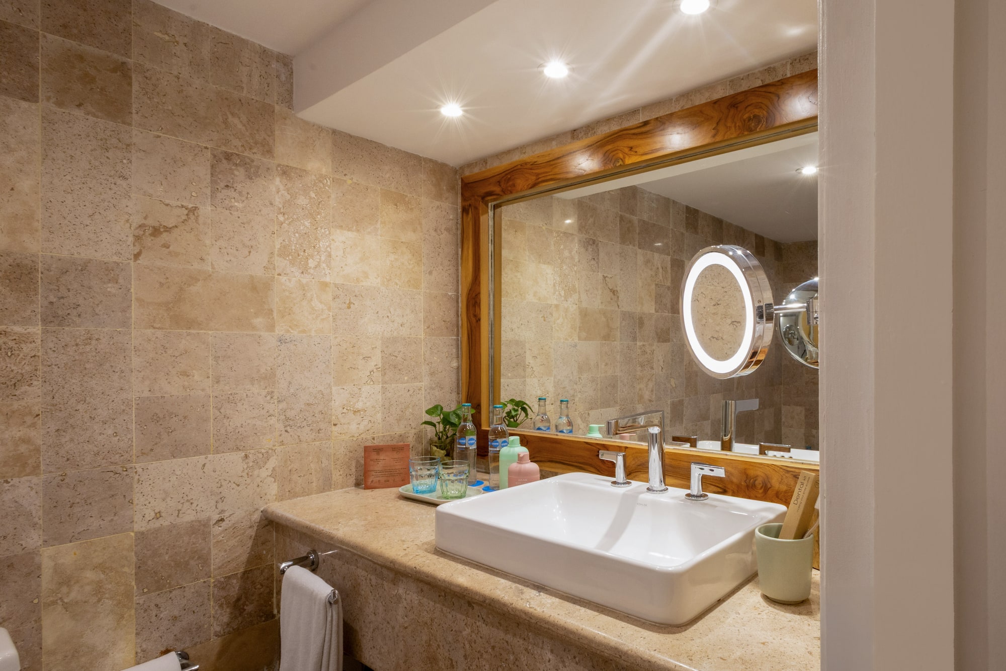 Baño moderno, tocador con lavabo blanco, espejo de madera y azulejos de piedra.