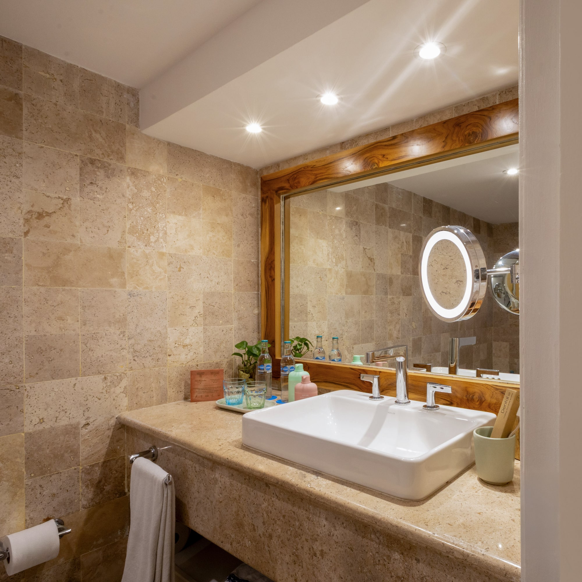 Baño moderno, tocador con lavabo blanco, espejo de madera y azulejos de piedra.