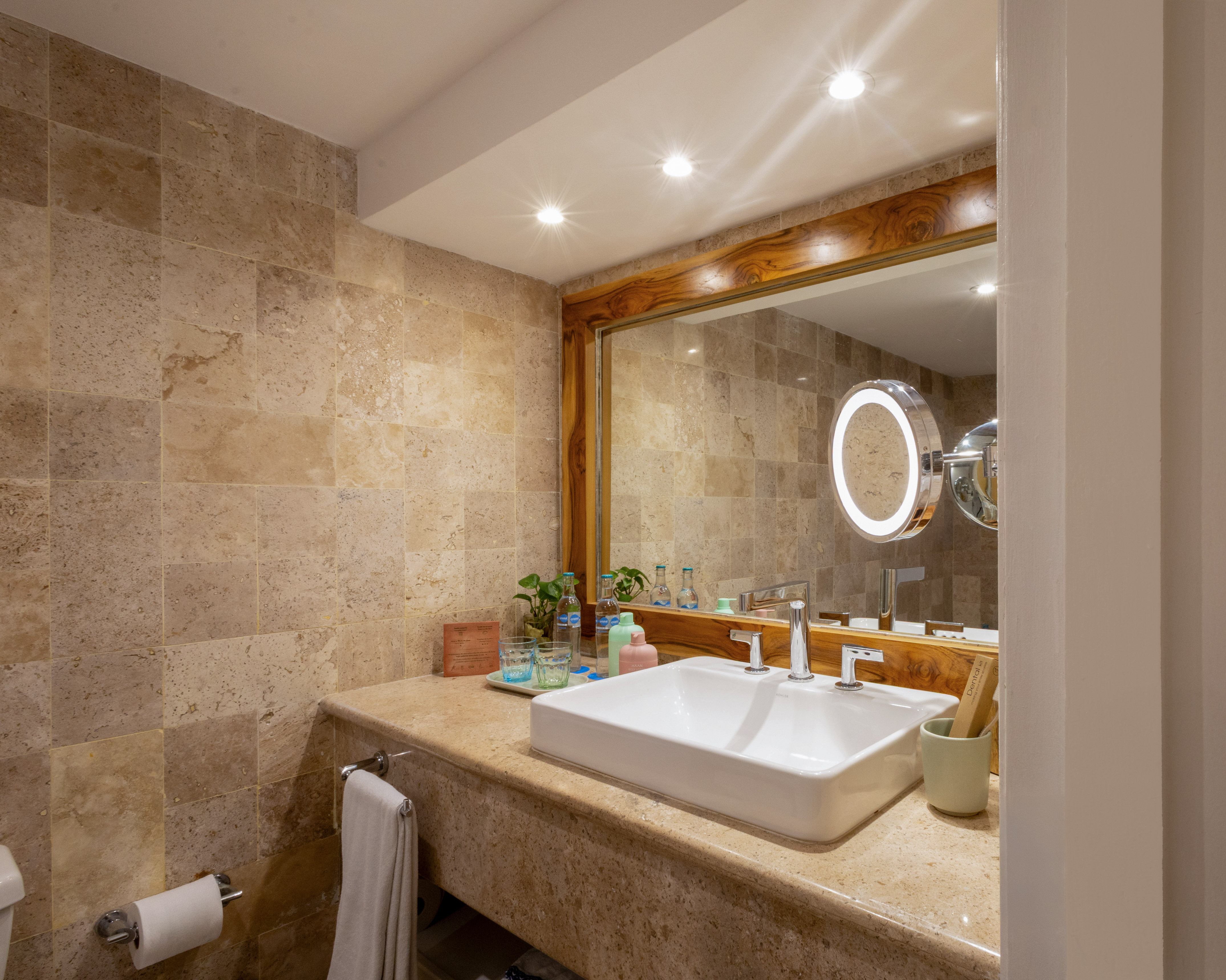 Baño moderno, tocador con lavabo blanco, espejo de madera y azulejos de piedra.