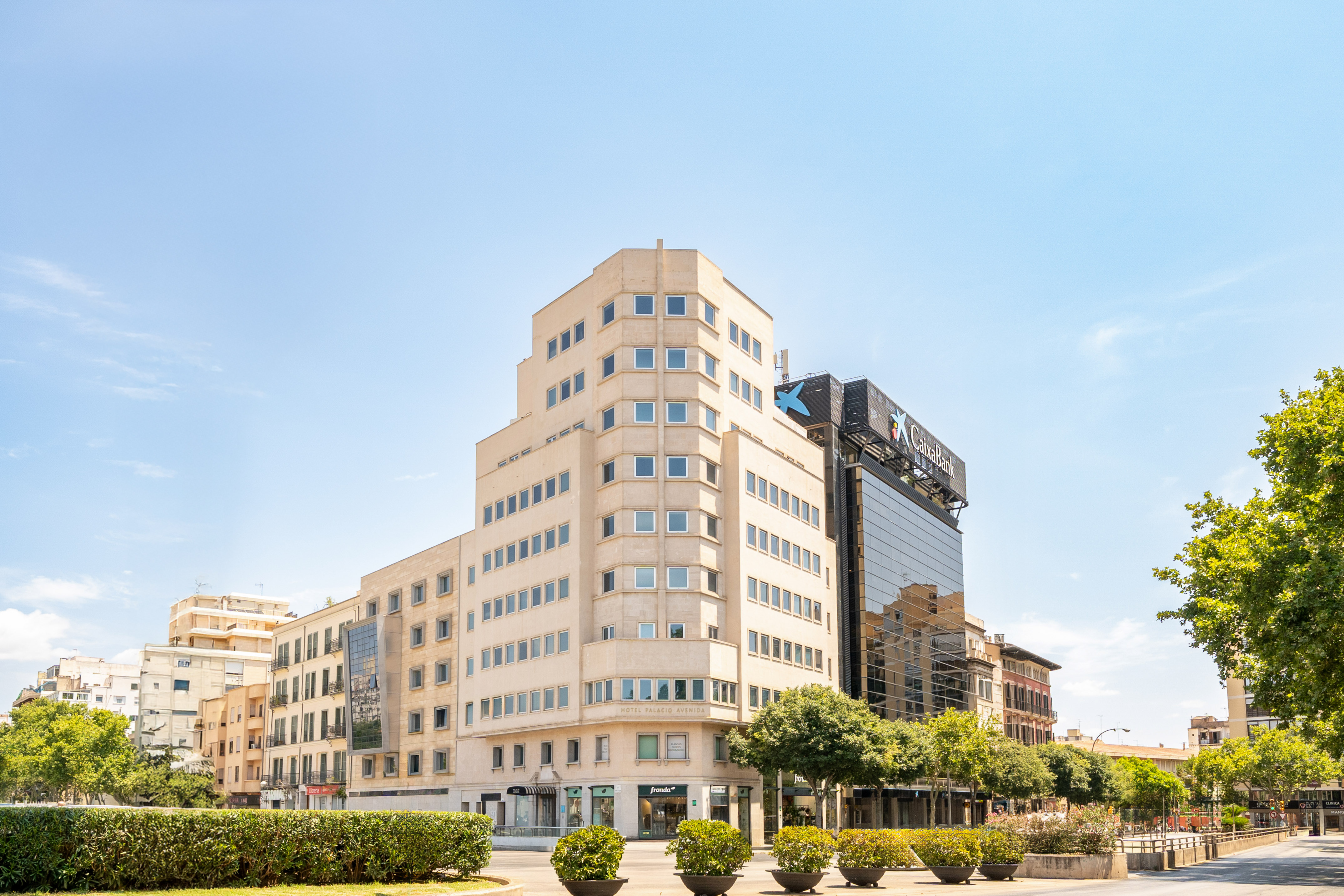 CaixaBank tower and Hotel Palacio Avenida on a bright urban street with trees.