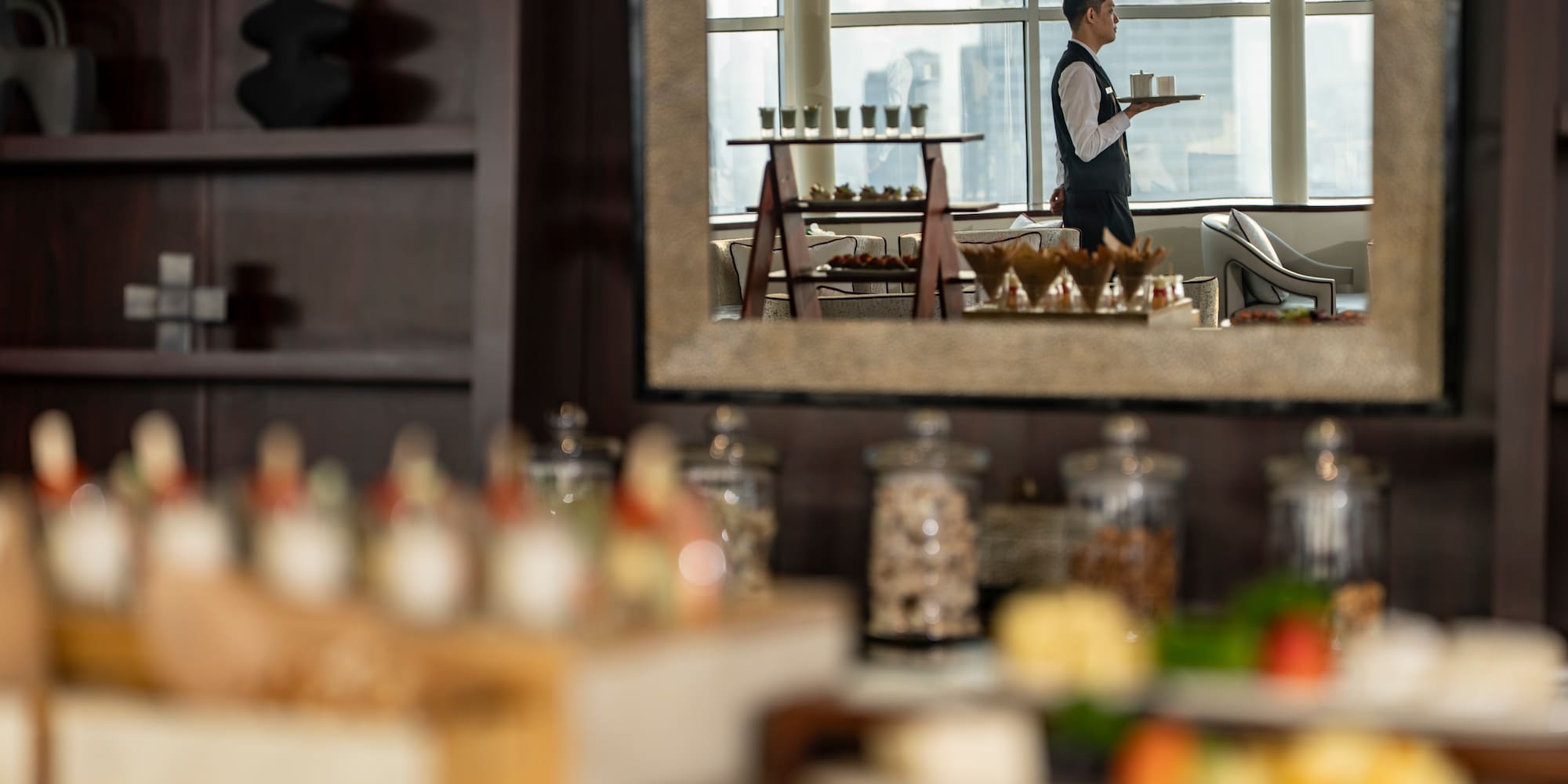 Waiter with tray in mirror reflection near hotel buffet spread.
