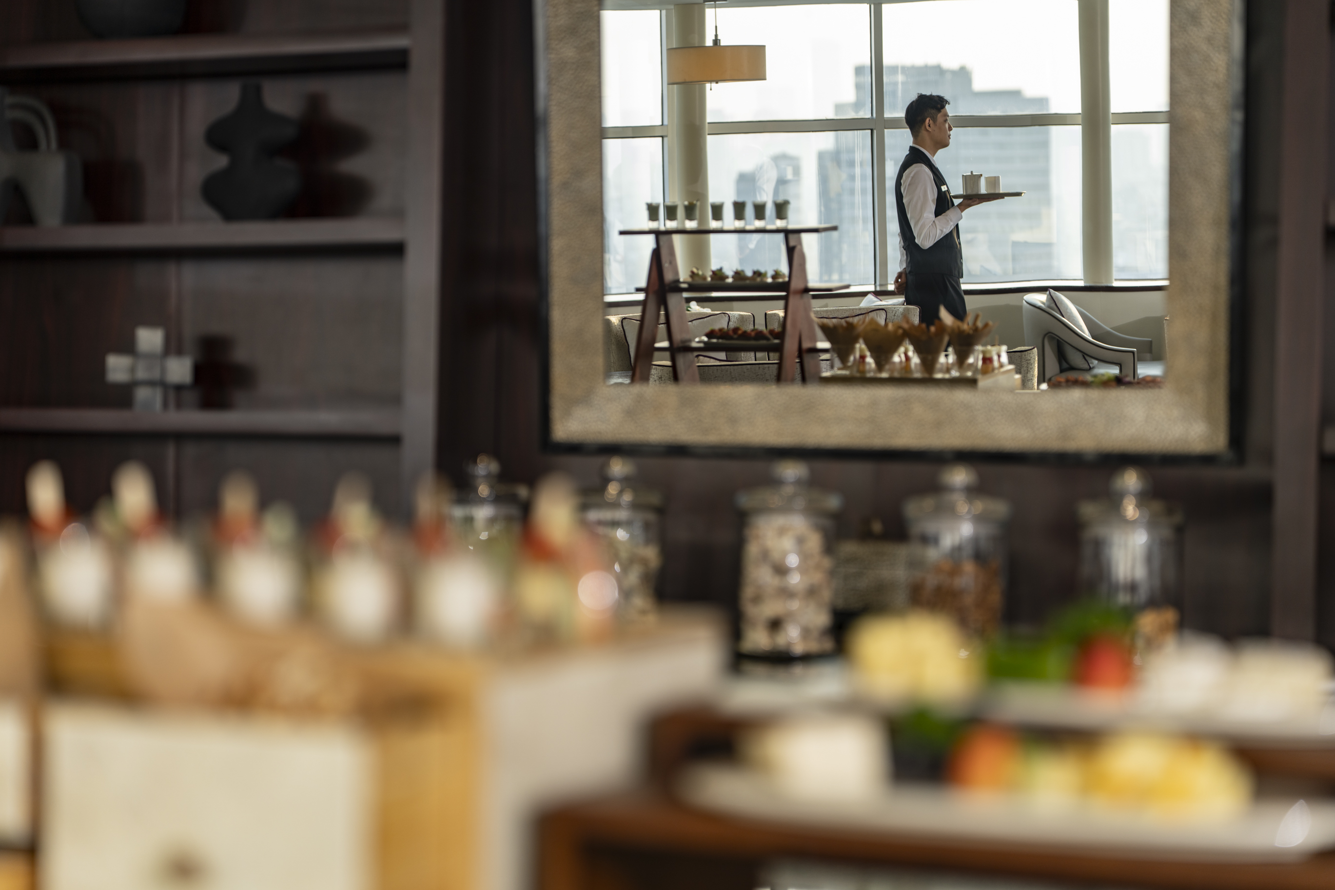 Waiter with tray in mirror reflection near hotel buffet spread.