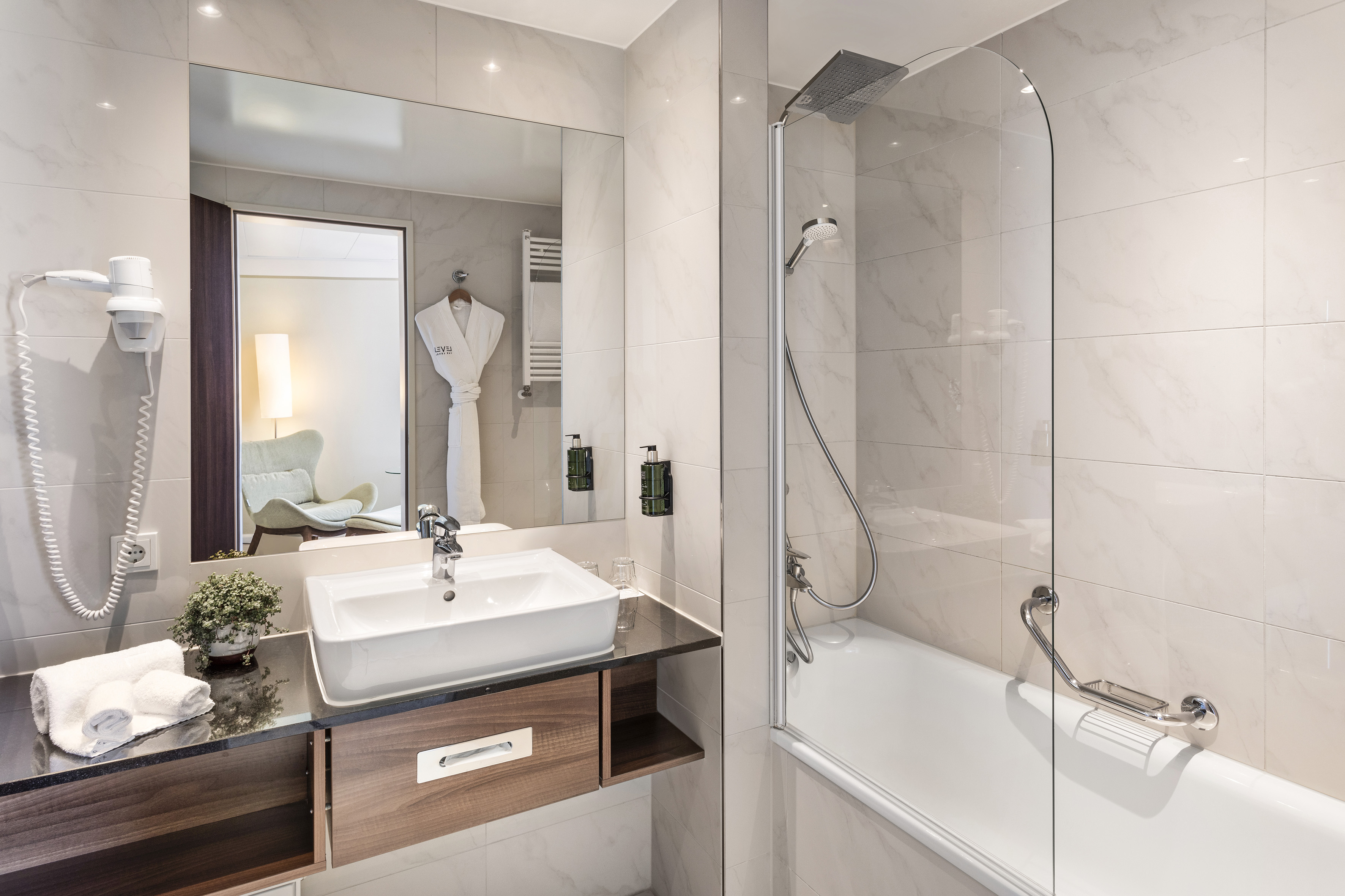 Modern hotel bathroom with white marble tiles, vanity, shower, and bathtub.