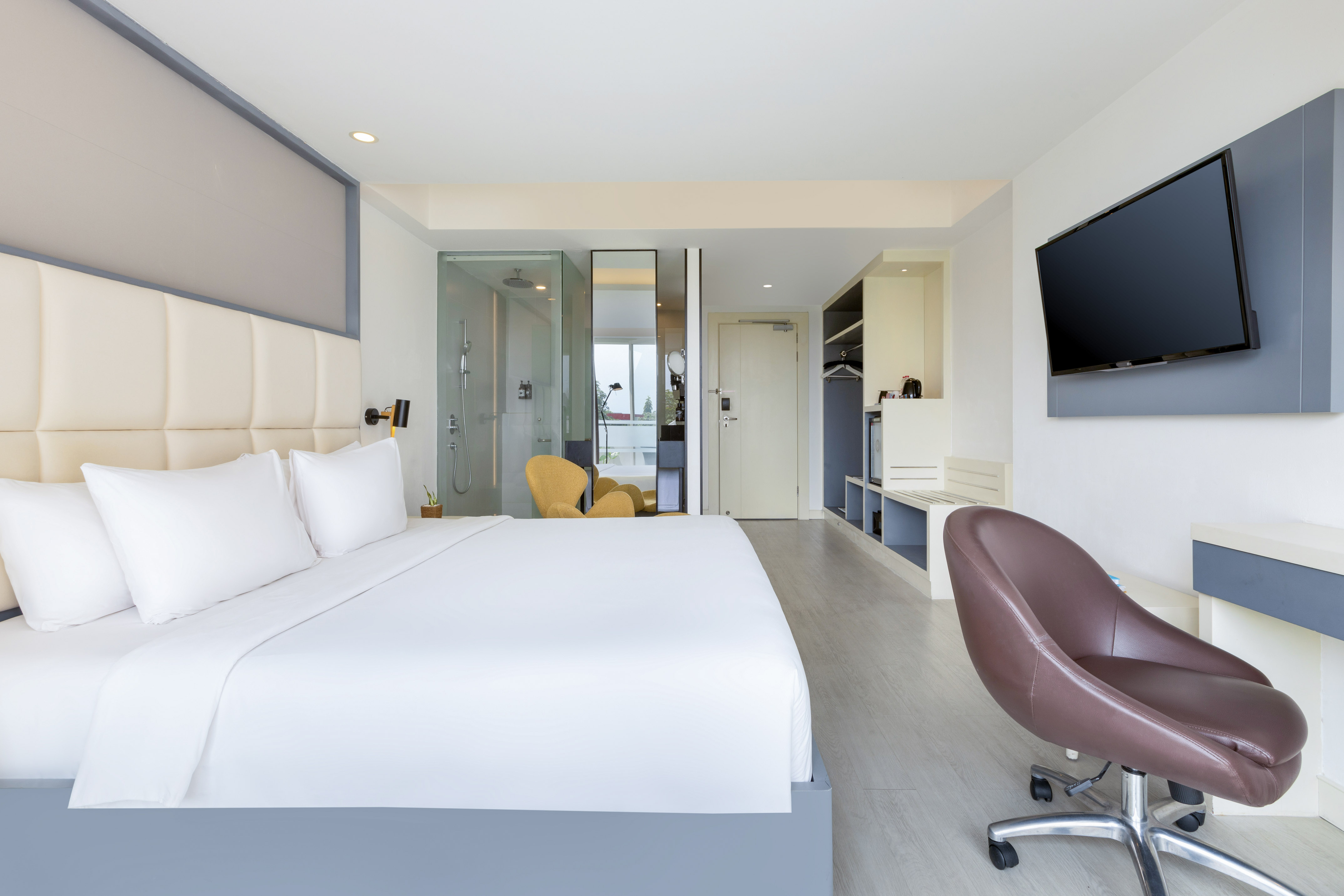 Modern hotel room: king bed, desk, TV, and glass-enclosed shower.