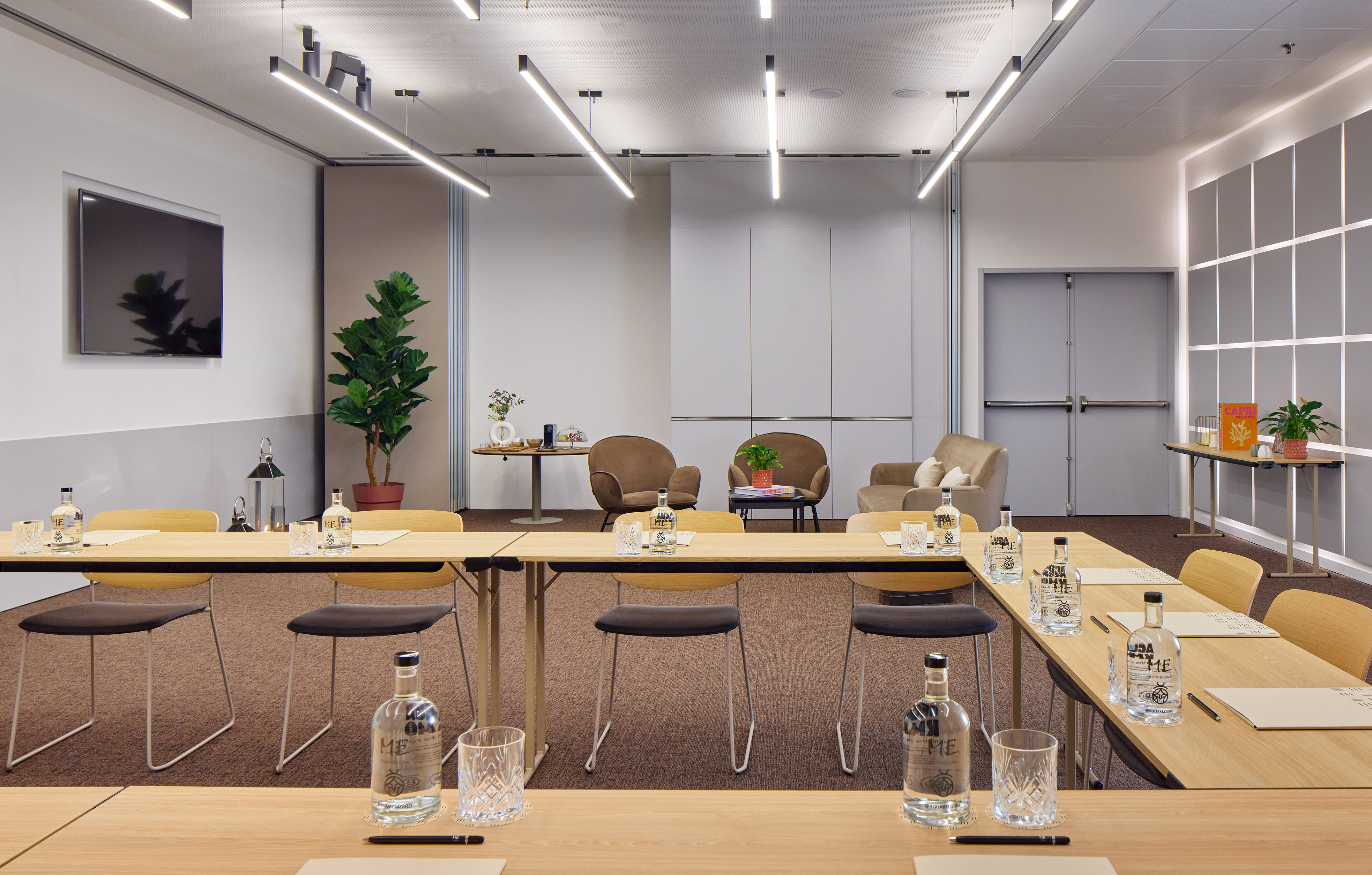 Flexible meeting room with tables, wall TV, and comfortable lounge area.