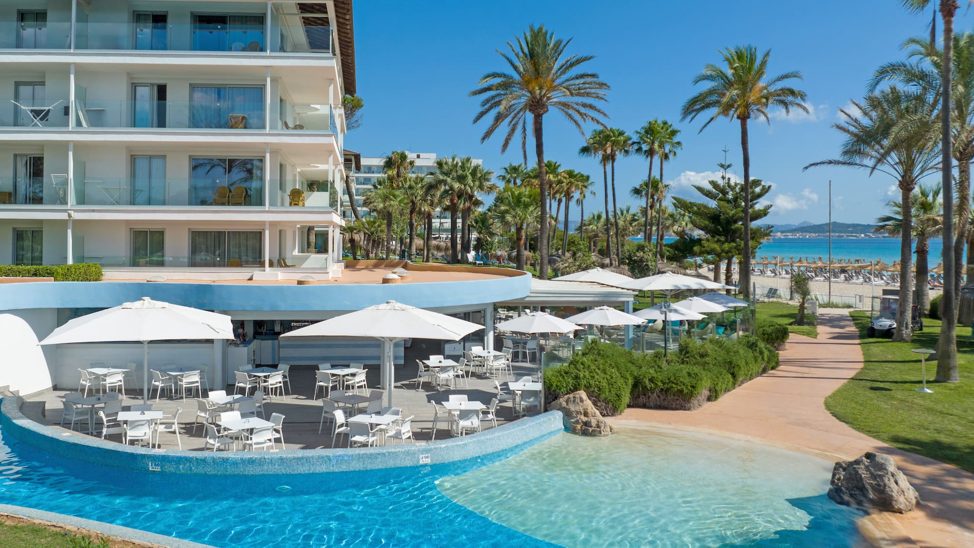 a swimming pool with tables and chairs in front of a building