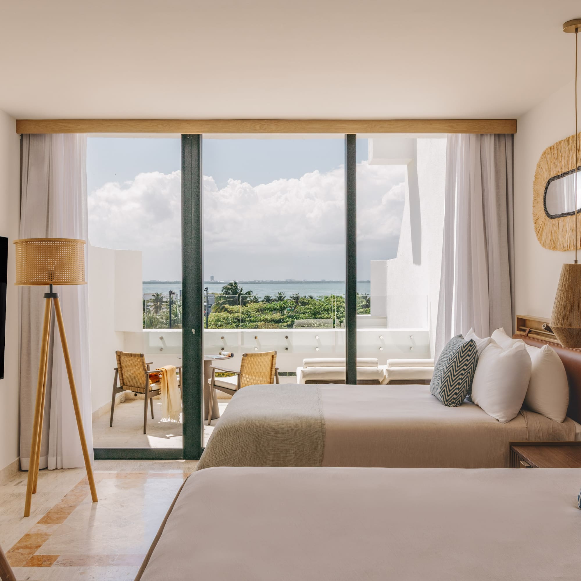 Modern hotel room with two beds, ocean view balcony, tropical decor.