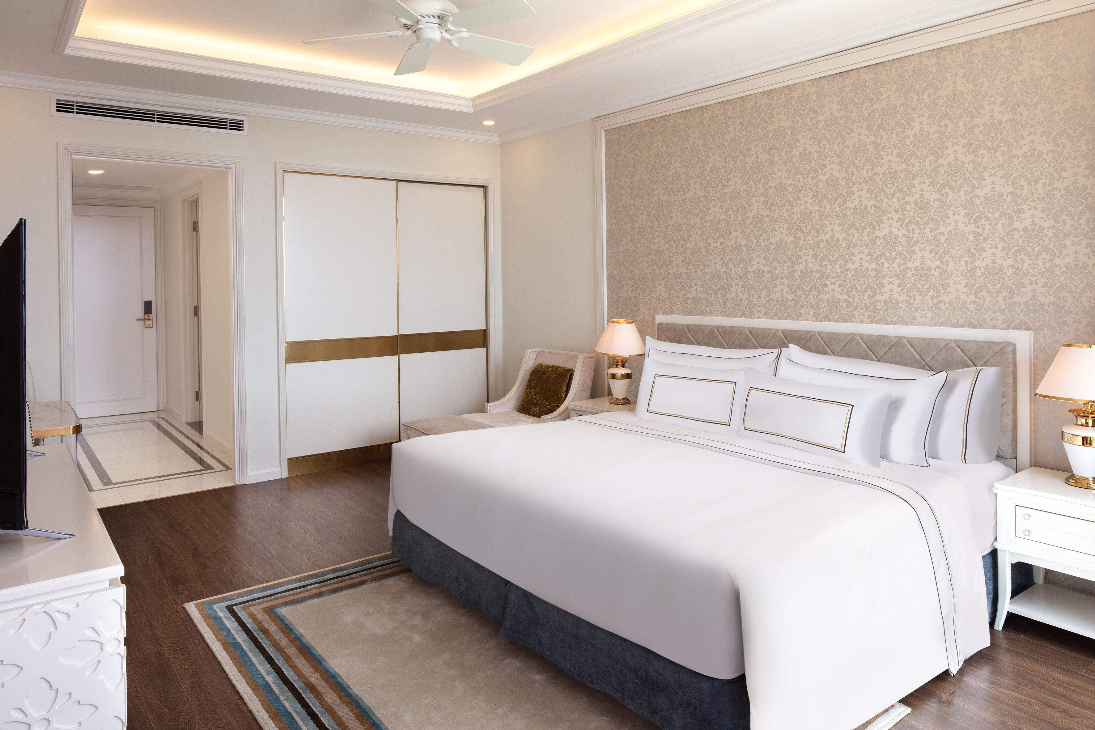 Luxury hotel bedroom with white king bed, patterned wallpaper, and wood floor.
