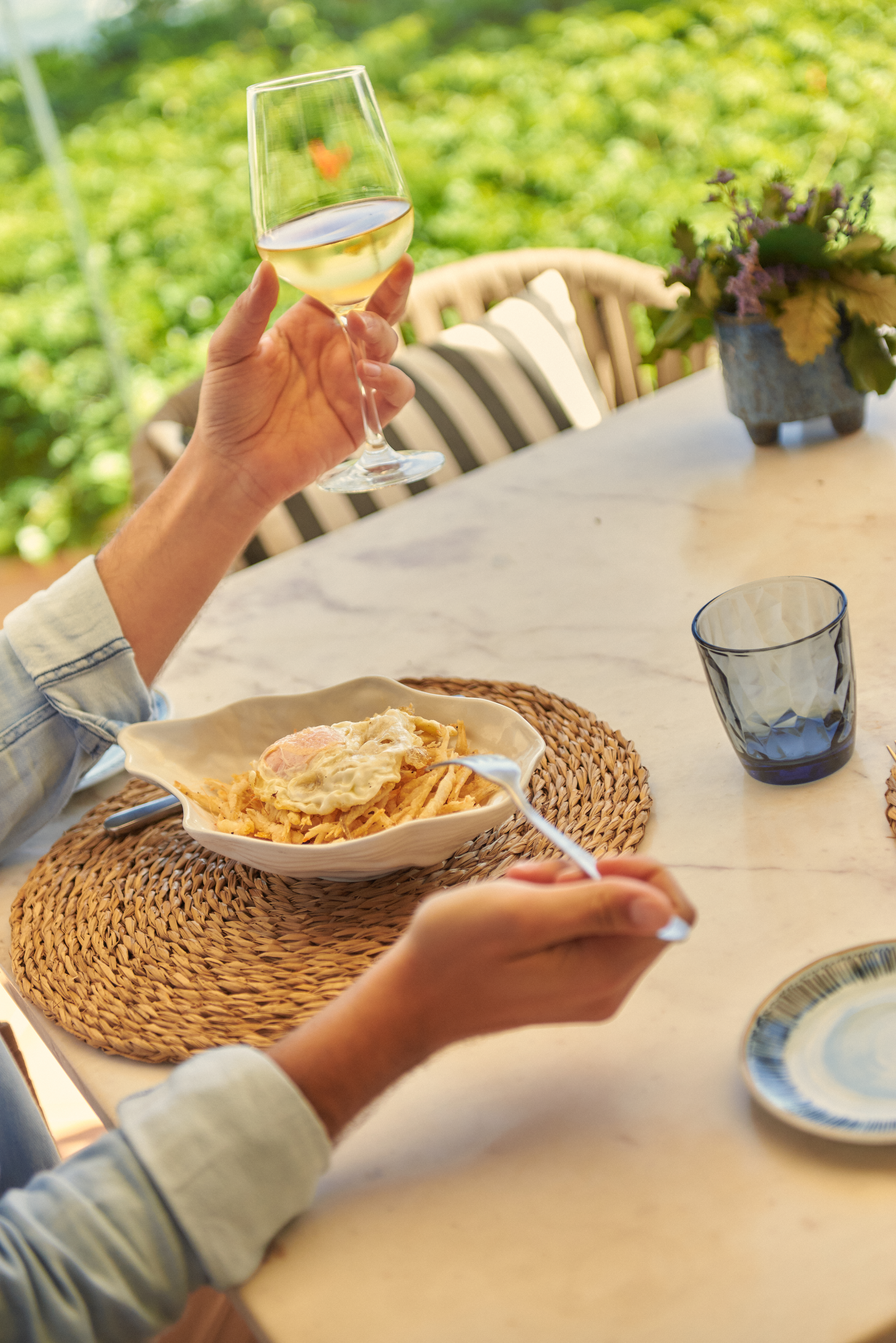 a person holding a glass of wine and a bowl of pasta
