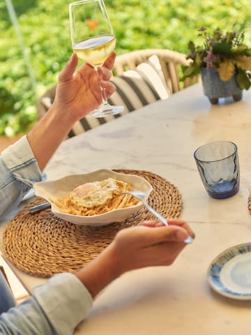 a person holding a glass of wine and a bowl of pasta