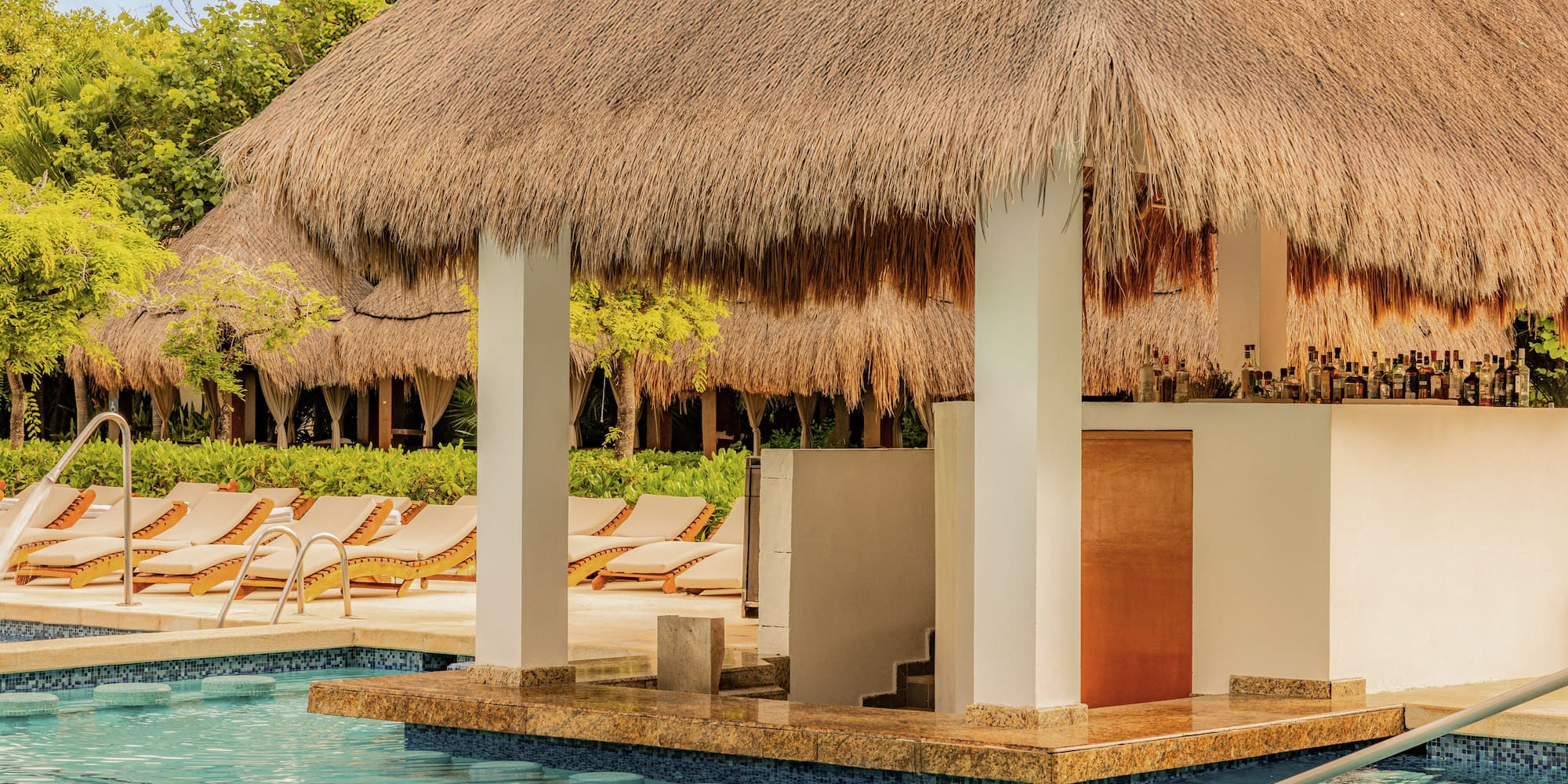 Thatched-roof swim-up bar with bottles by a tropical resort pool.