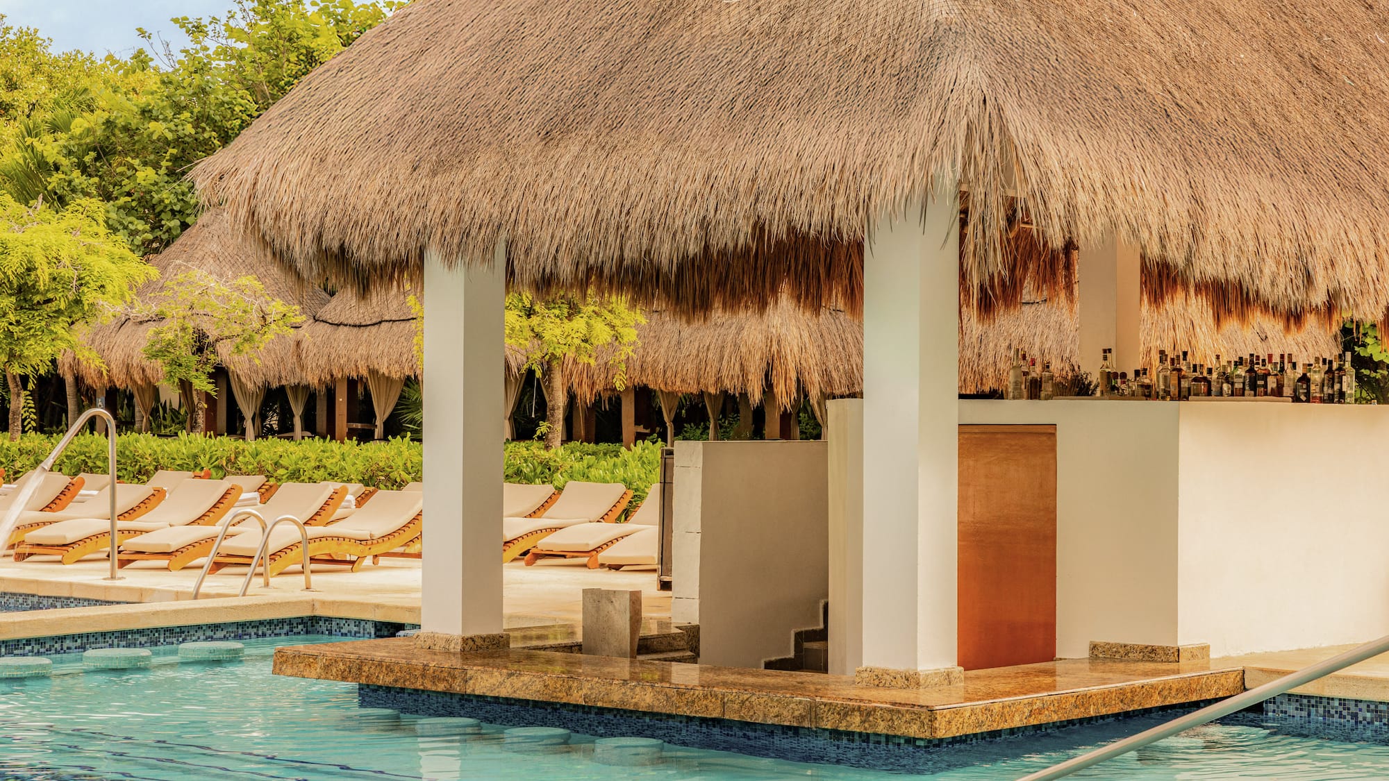 Thatched-roof swim-up bar with bottles by a tropical resort pool.
