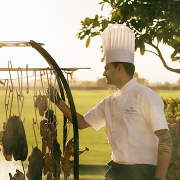 Chef cooking on the asado grill, with view of the polo field