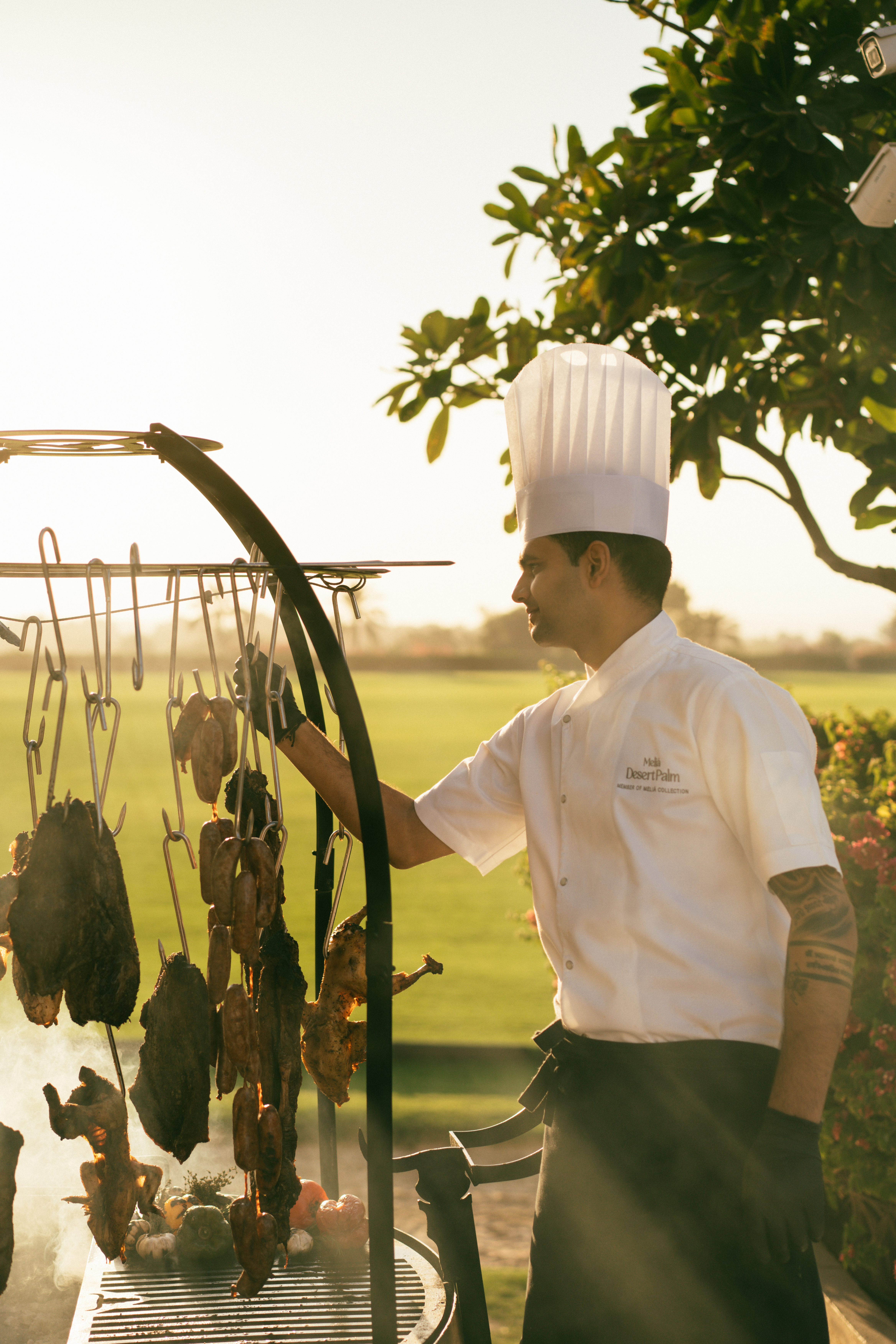 Chef cooking hanging meats on an outdoor asado grill at Melia Desert Palm.