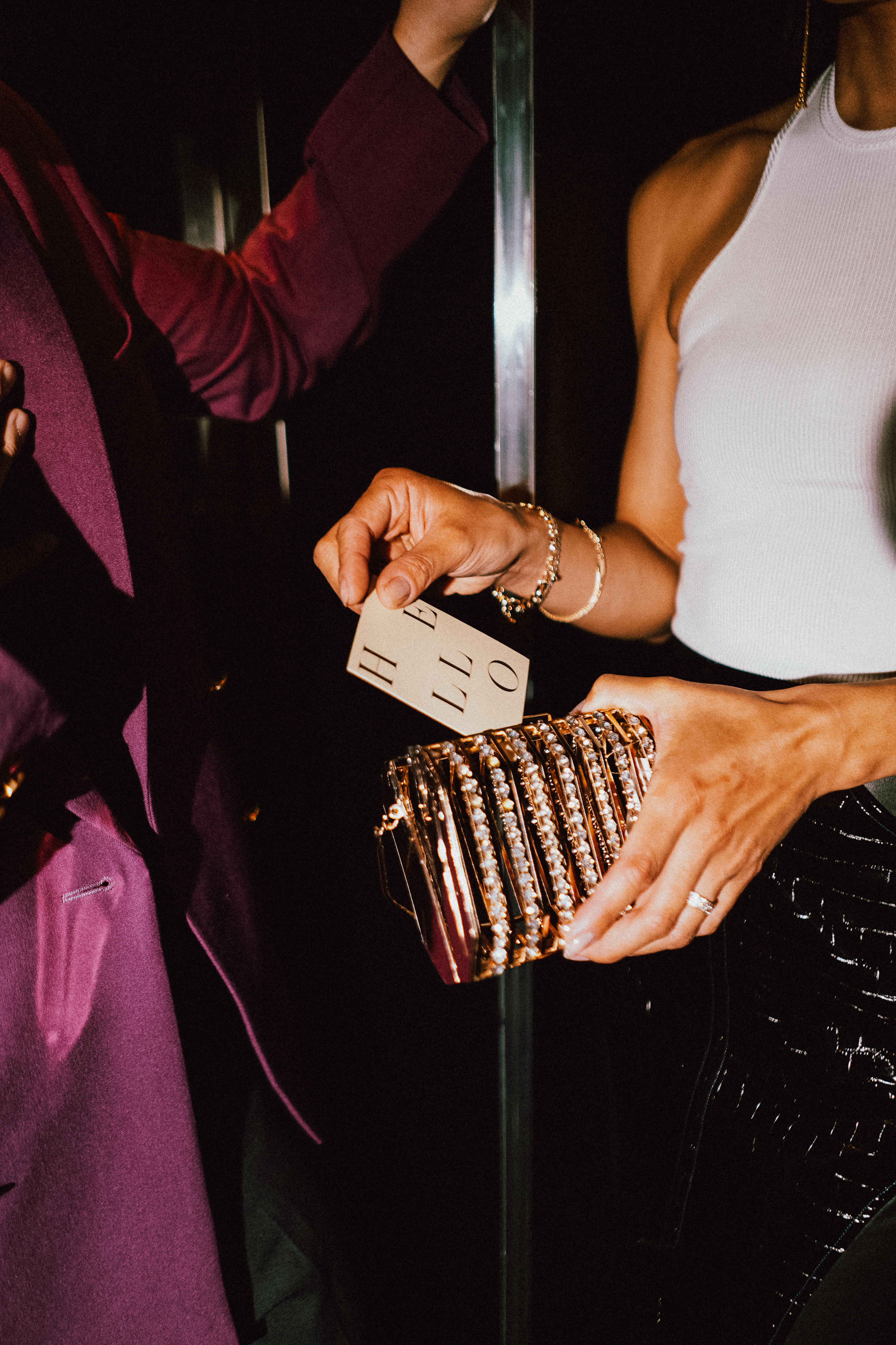 Woman's hand with 'HELLO' card and sparkling gold clutch at an event.