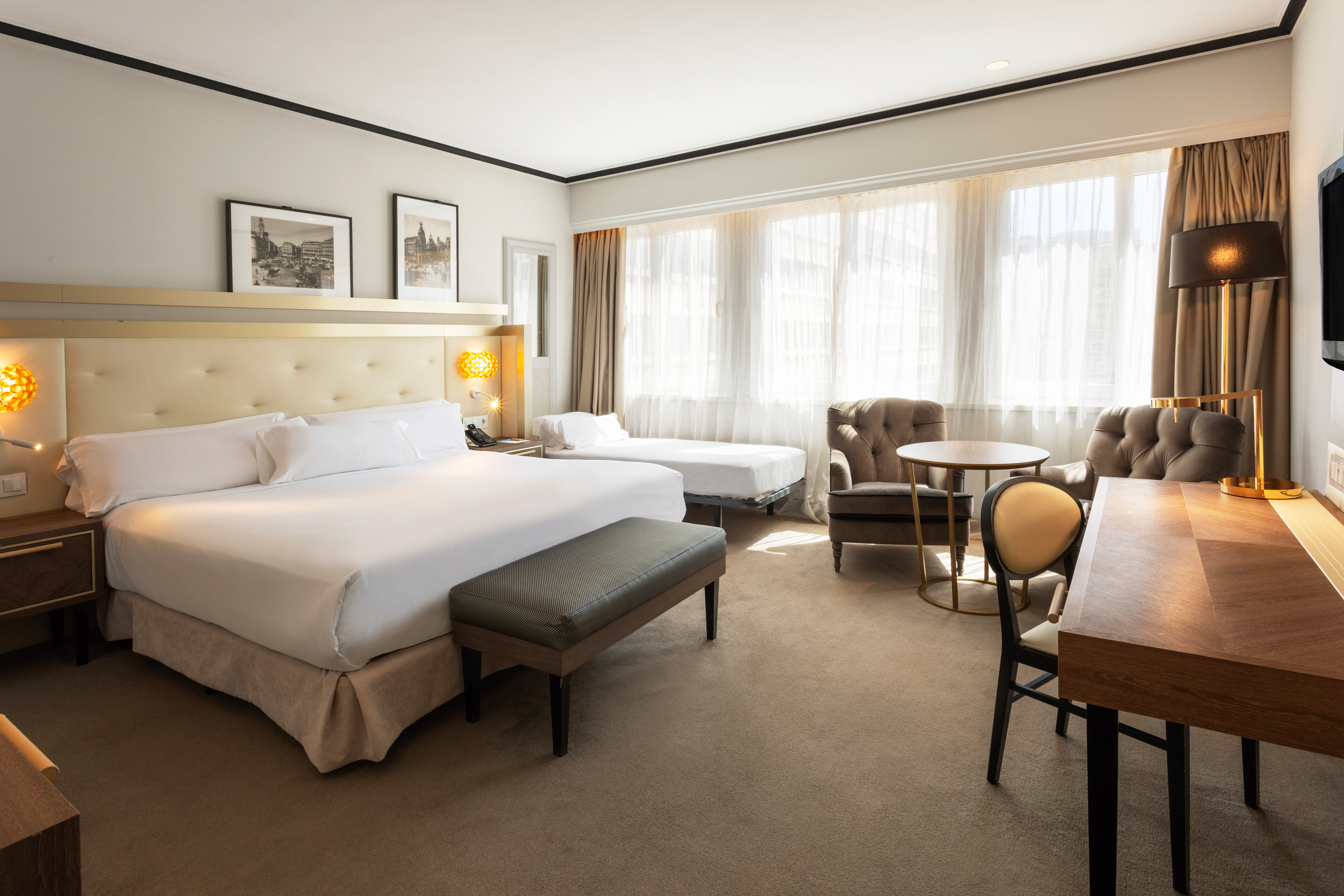 Hotel guest room: king bed, twin bed, desk, and armchairs by a bright window.