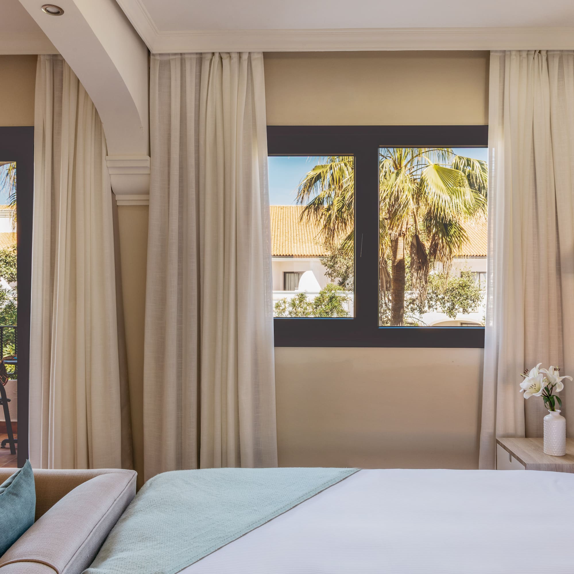 Hotel room with bed, sofa, balcony, and tropical palm tree view.