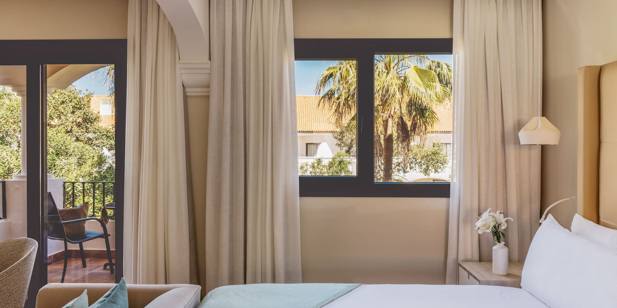 Hotel room with bed, sofa, balcony, and tropical palm tree view.