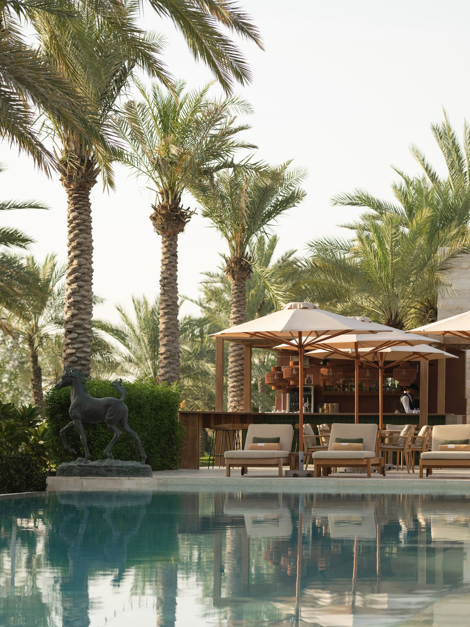 Luxury resort pool with palm trees, lounge chairs, umbrellas, and poolside bar.