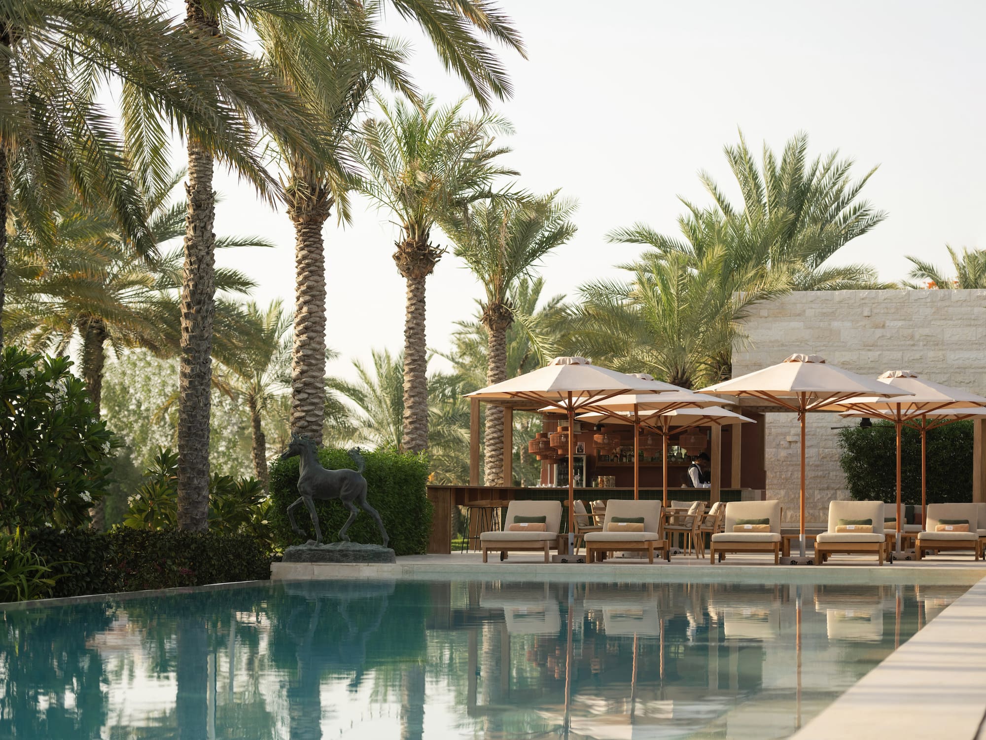 Luxury resort pool with palm trees, lounge chairs, umbrellas, and poolside bar.