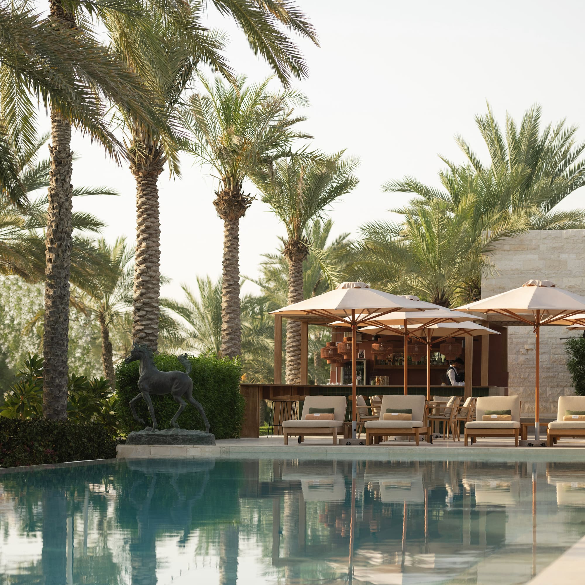 Luxury resort pool with palm trees, lounge chairs, umbrellas, and poolside bar.
