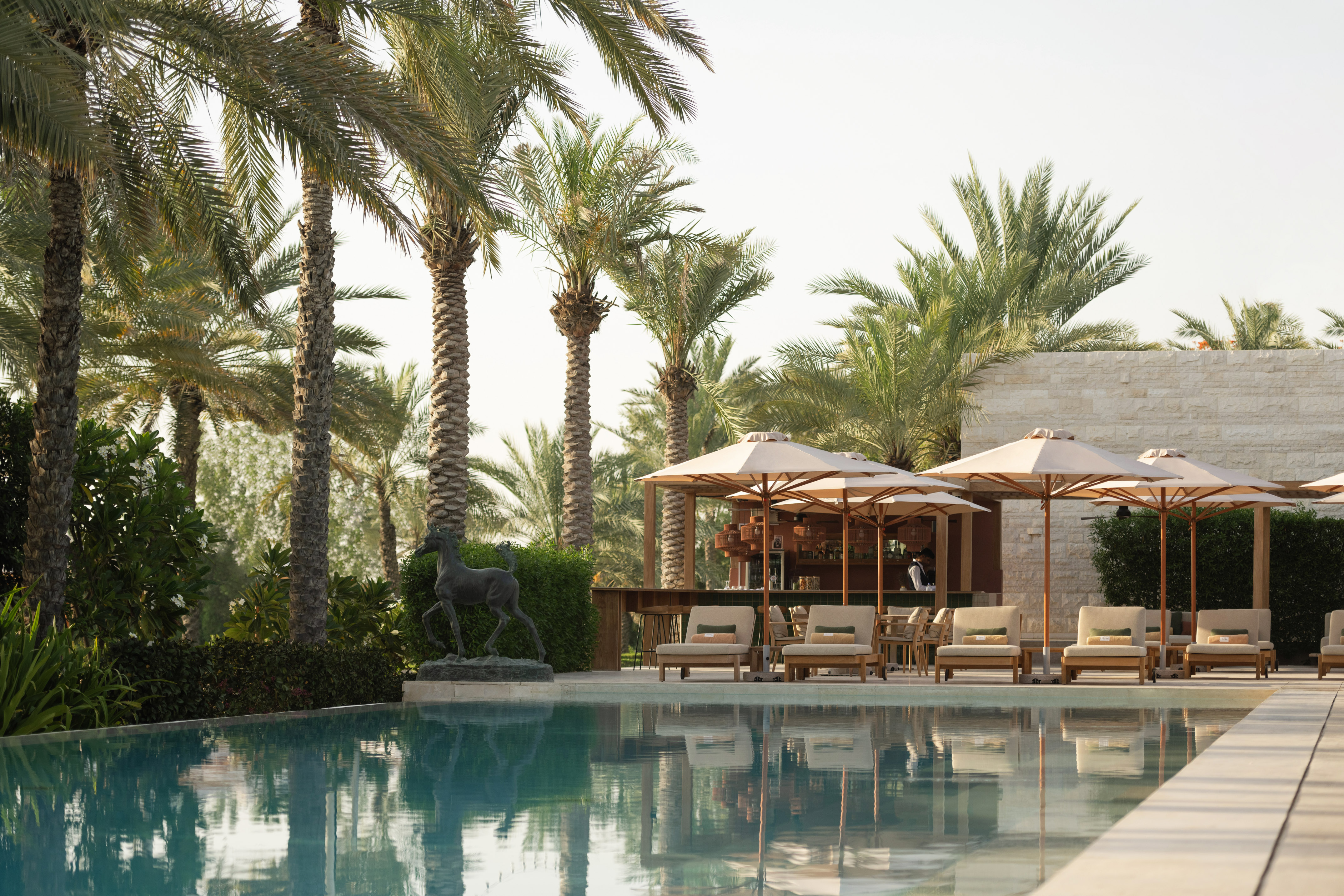 Luxury resort pool with palm trees, lounge chairs, umbrellas, and poolside bar.