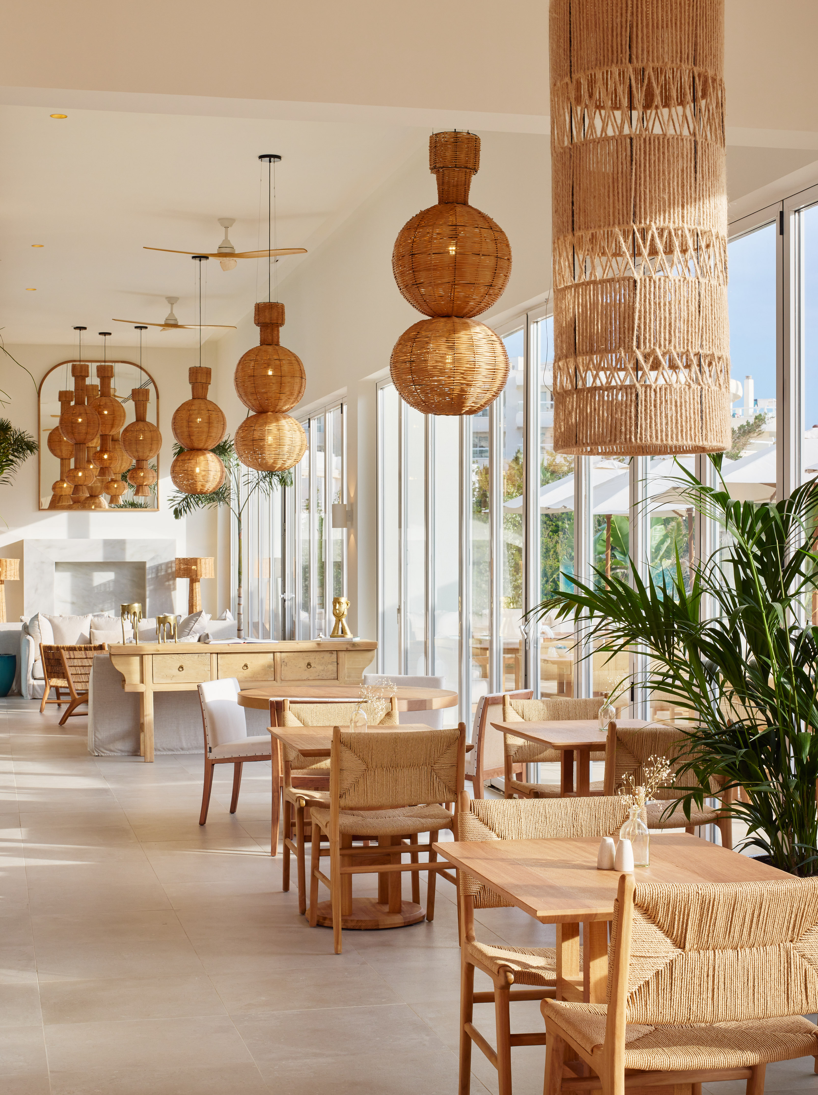 Sunny resort dining area with woven rattan lamps, wood tables, and plants.