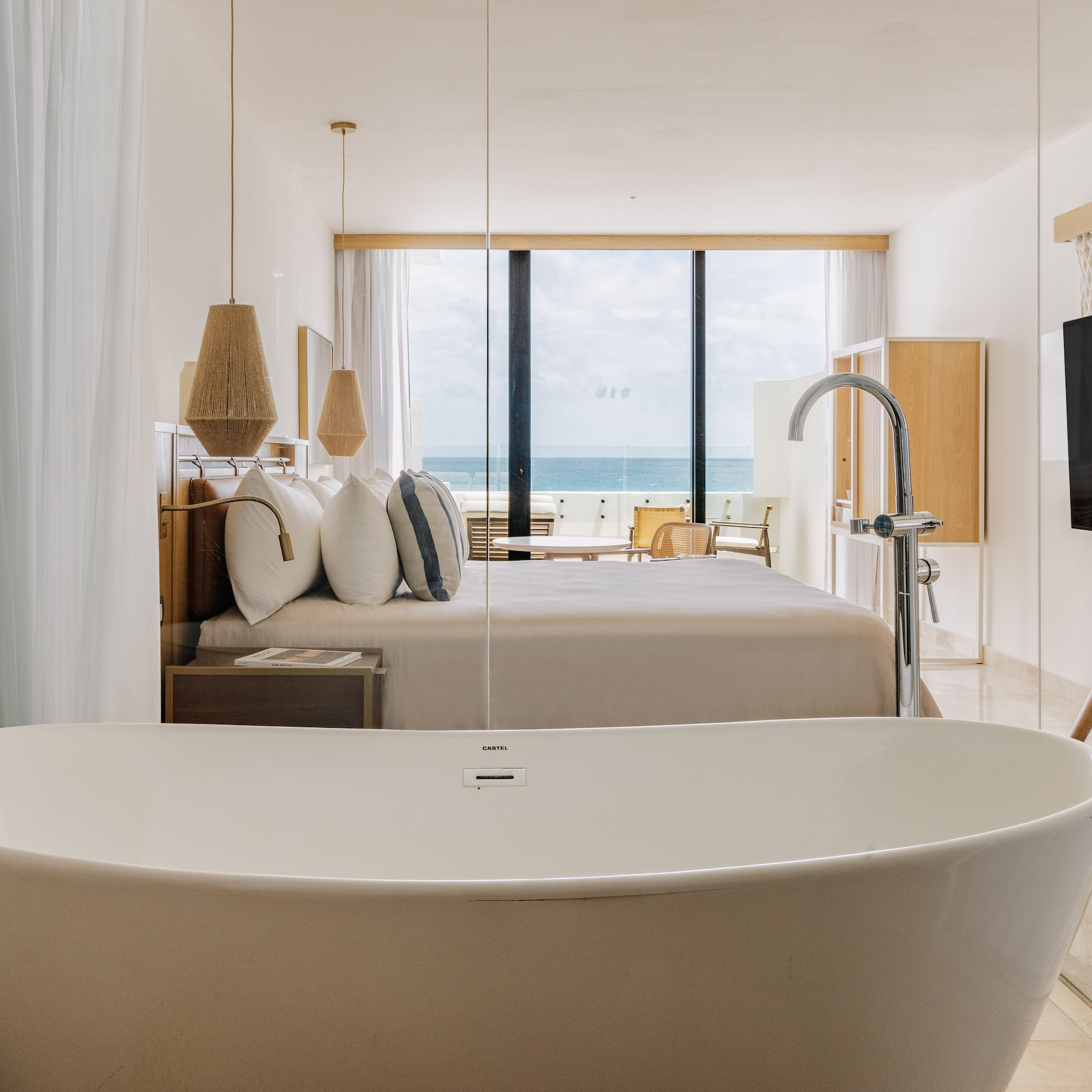 Modern ocean view hotel suite with freestanding bathtub and king bed.
