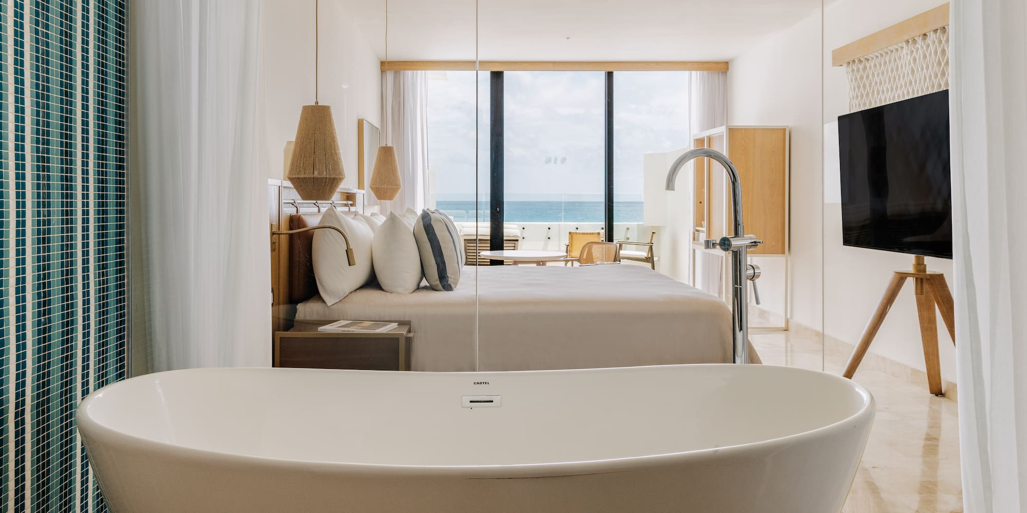 Modern ocean view hotel suite with freestanding bathtub and king bed.
