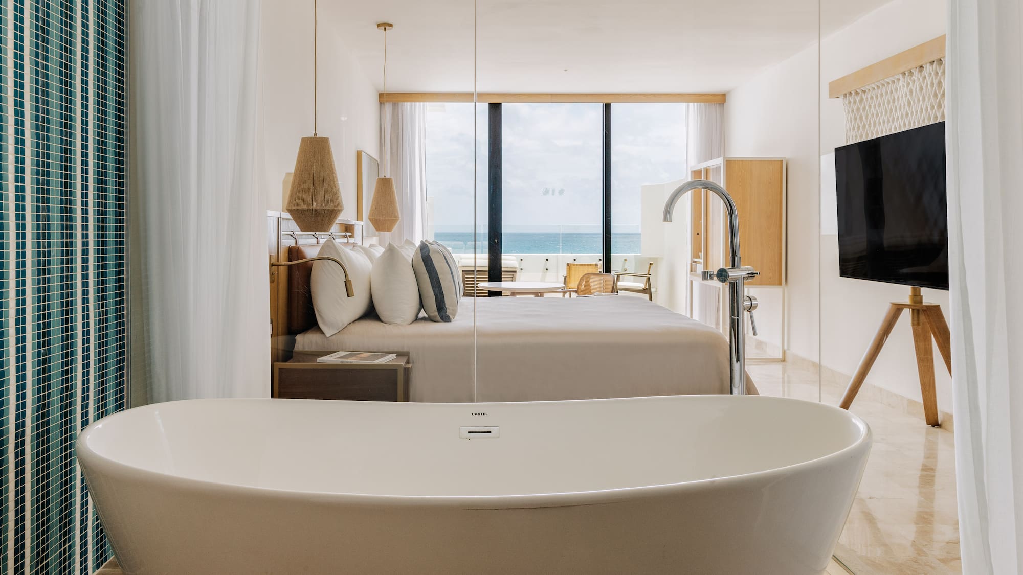 Modern ocean view hotel suite with freestanding bathtub and king bed.