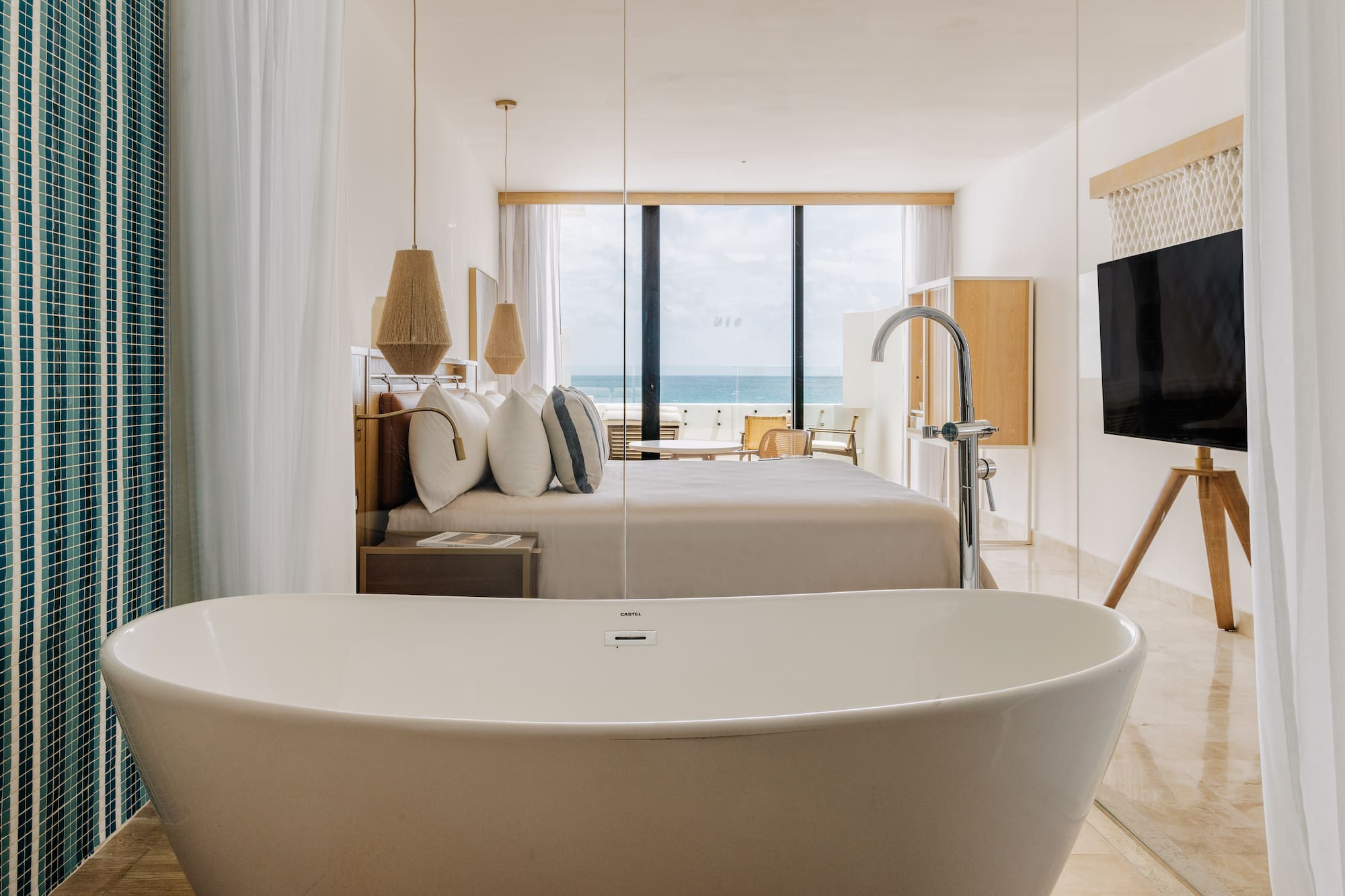 Modern ocean view hotel suite with freestanding bathtub and king bed.