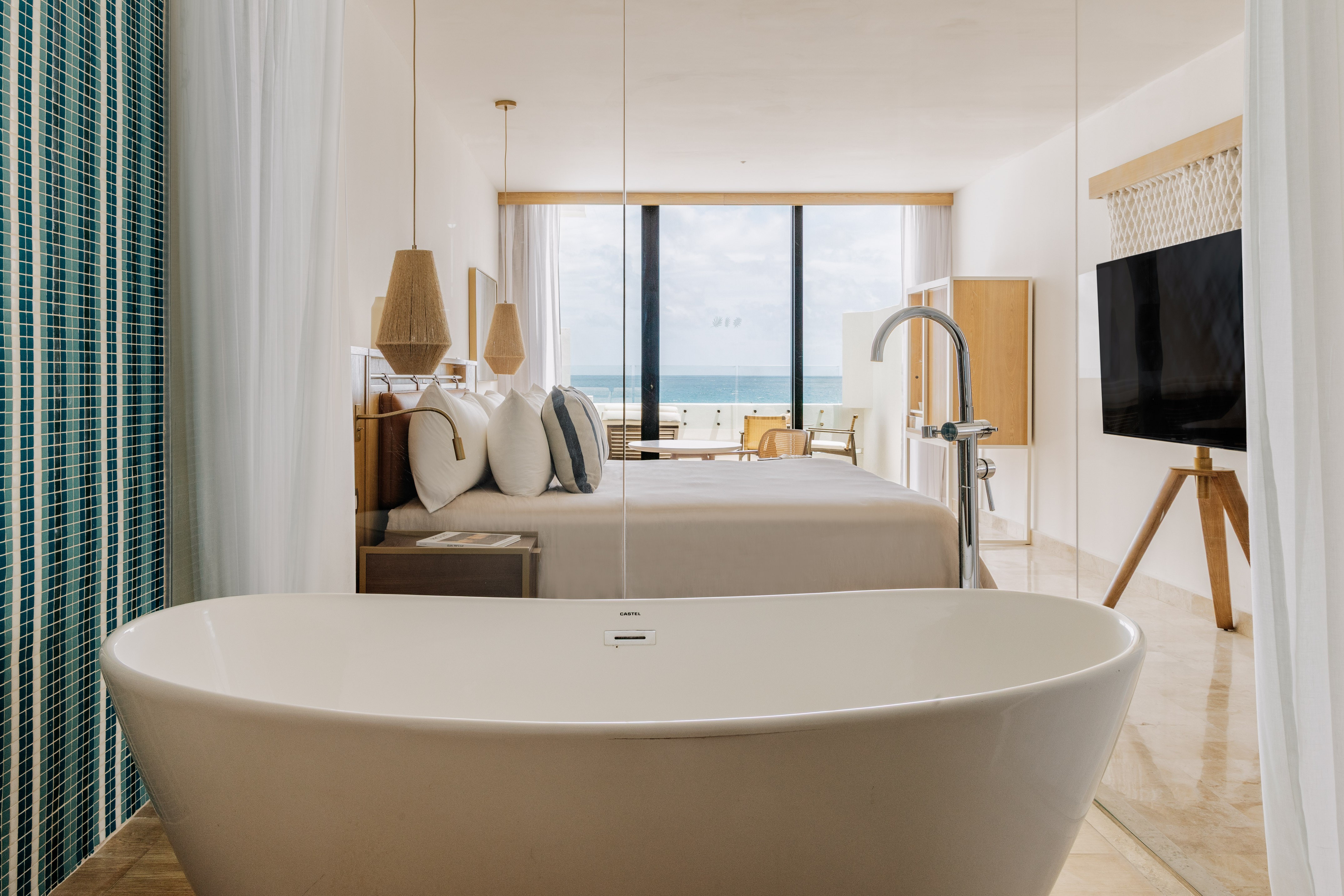 Modern ocean view hotel suite with freestanding bathtub and king bed.