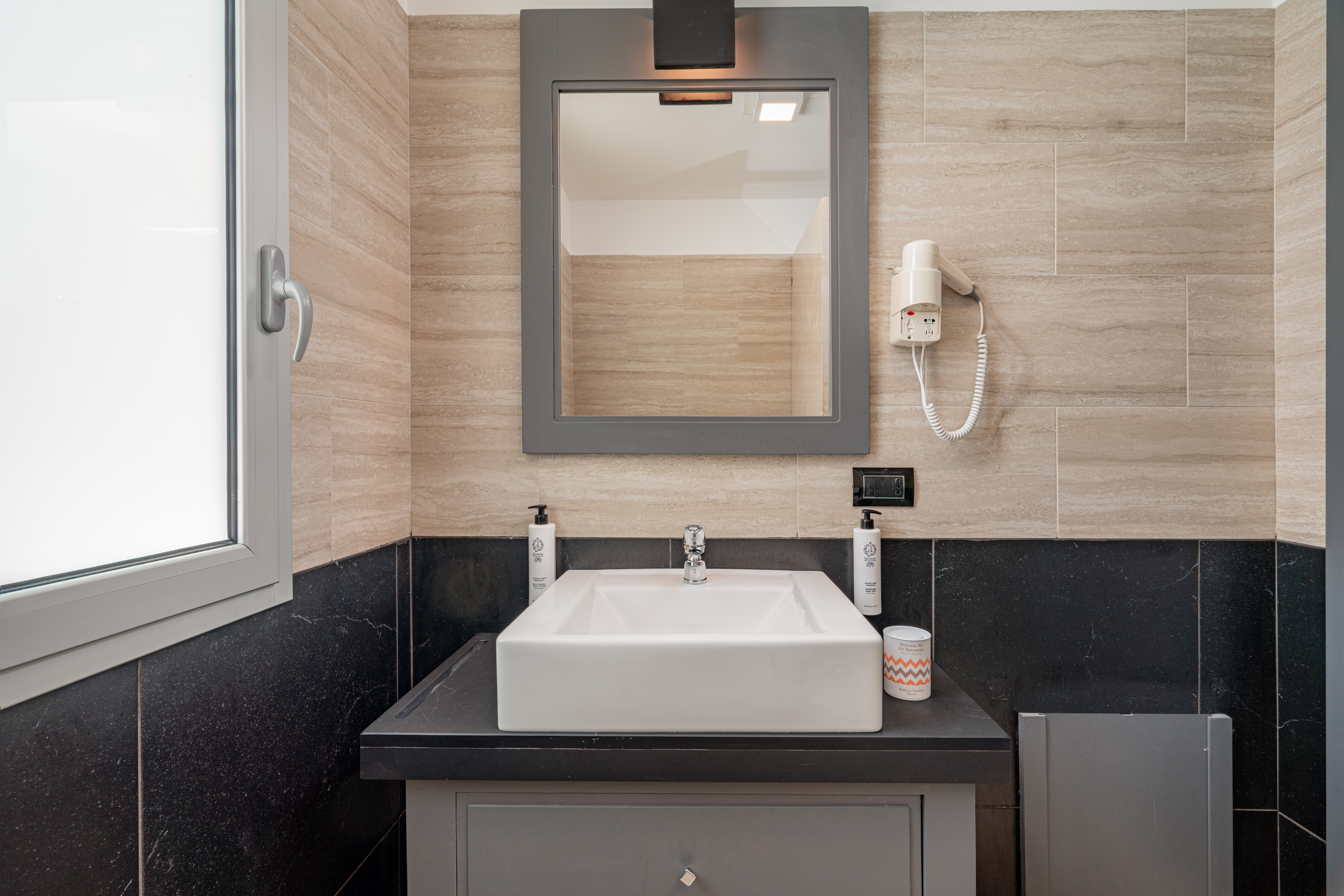 Modern bathroom vanity, white sink, gray mirror, beige/black tiles, hairdryer.