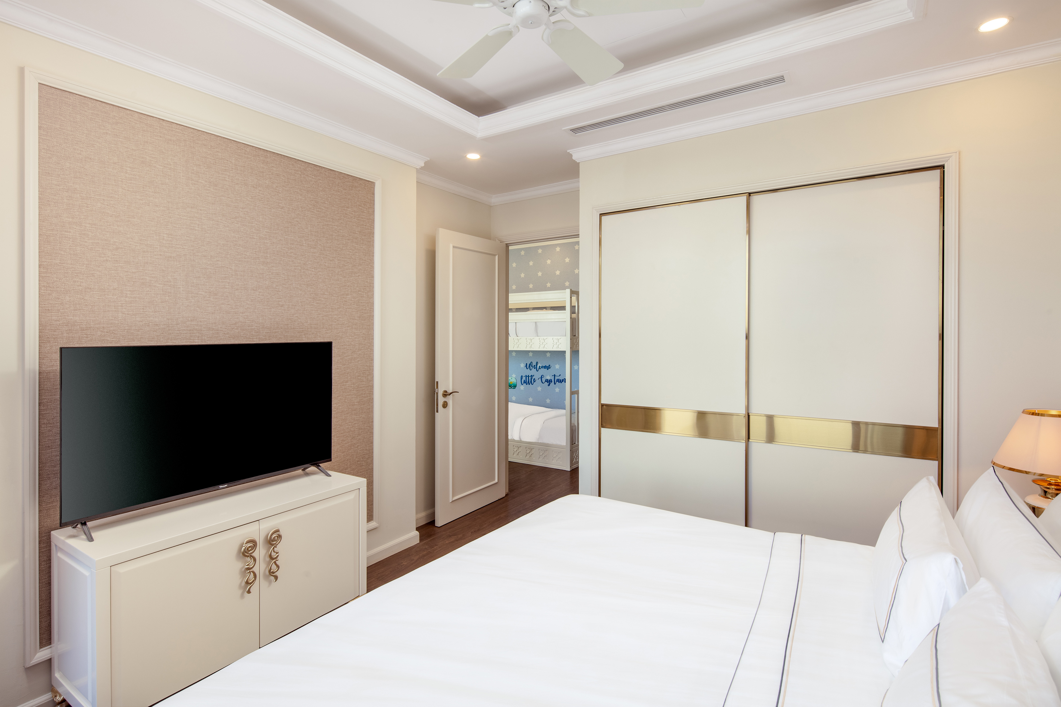 Modern bedroom with white bed, TV, and connecting kids' bunk room.