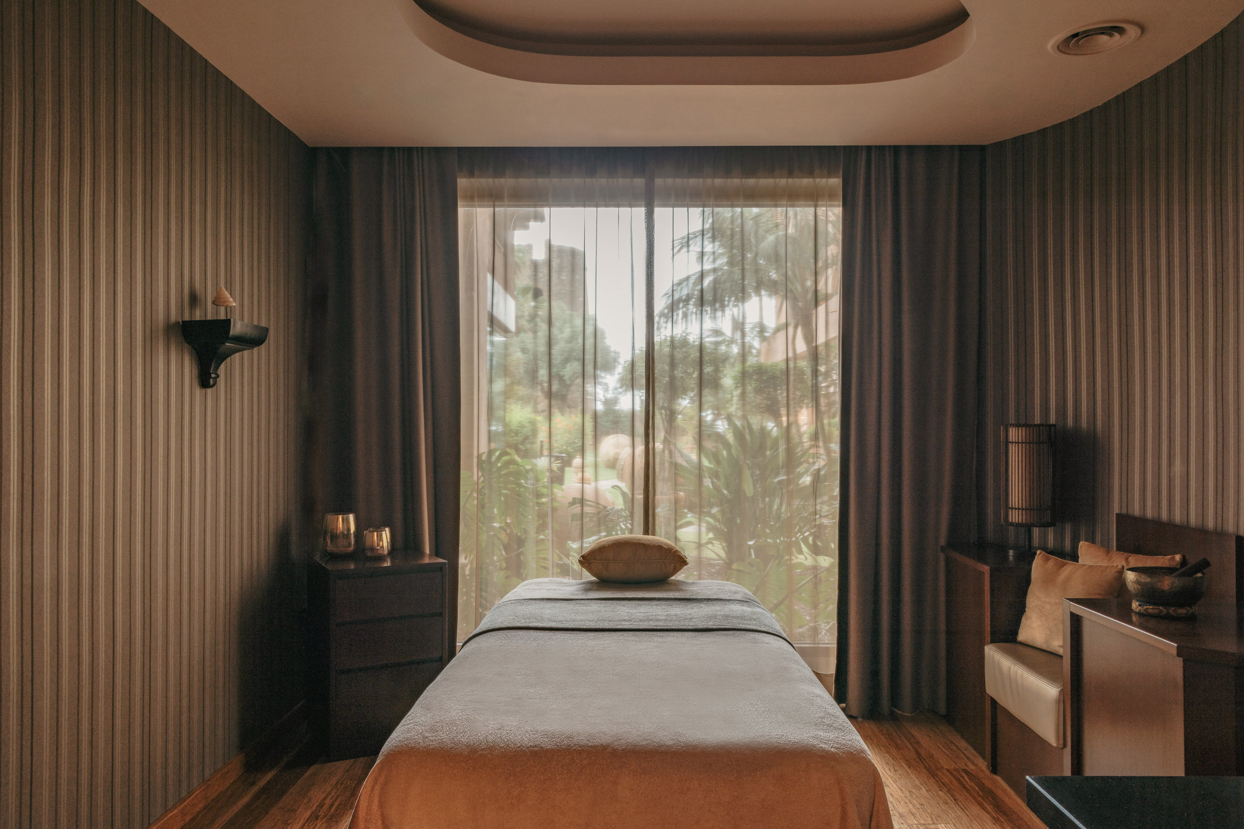 Luxury spa treatment room with massage table, garden view, and elegant decor.